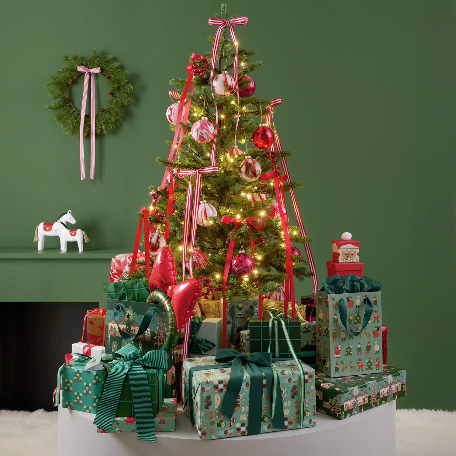 Paper Poetry bande tissée diagonale 50mm 3m Couleur Vert from Rico Design Weihnachtlich dekorierter Raum mit einem geschmückten Baum und Geschenken. Das Geschenkpapier von Rico Design, "Paper Poetry Weihnachtsmarkt Mix", zeigt festliche Muster in verschiedenen Farben.