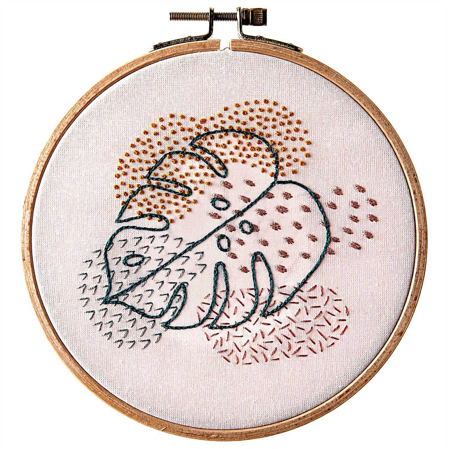 Stickpackung Slow Evenings Monstera Bild Ø 15,5cm zeigt ein gesticktes Monstera-Motiv in Erdtönen auf hellem Stoff, eingerahmt in einem Holzring.