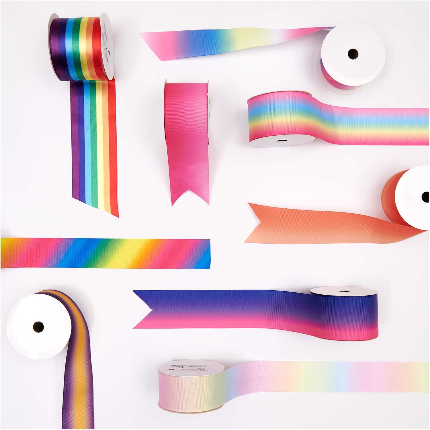 Dekoband mehrfarbig 5cm 3m von Rico Design Dekoband mehrfarbig 5cm 3m: Verschiedene bunte Bänder von Rico Design auf weißen Rollen arrangiert.