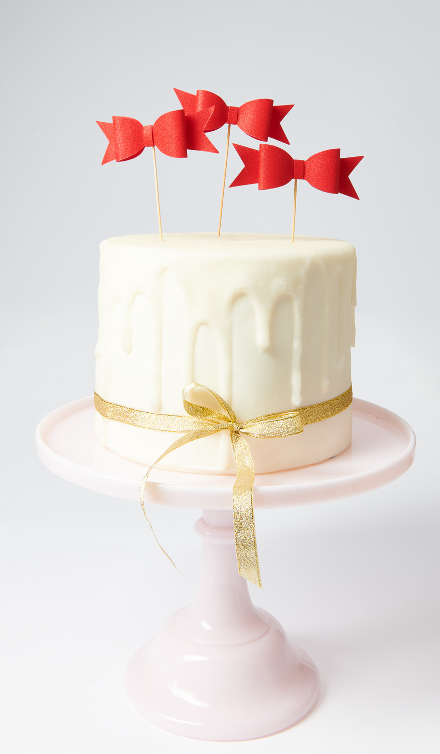 Picker Schleife Rot 10,5x13,5cm 6 Stück von Rico Design Picker Schleife Rot auf einer weißen Torte mit goldener Schleife, präsentiert auf einem rosa Tortenständer.