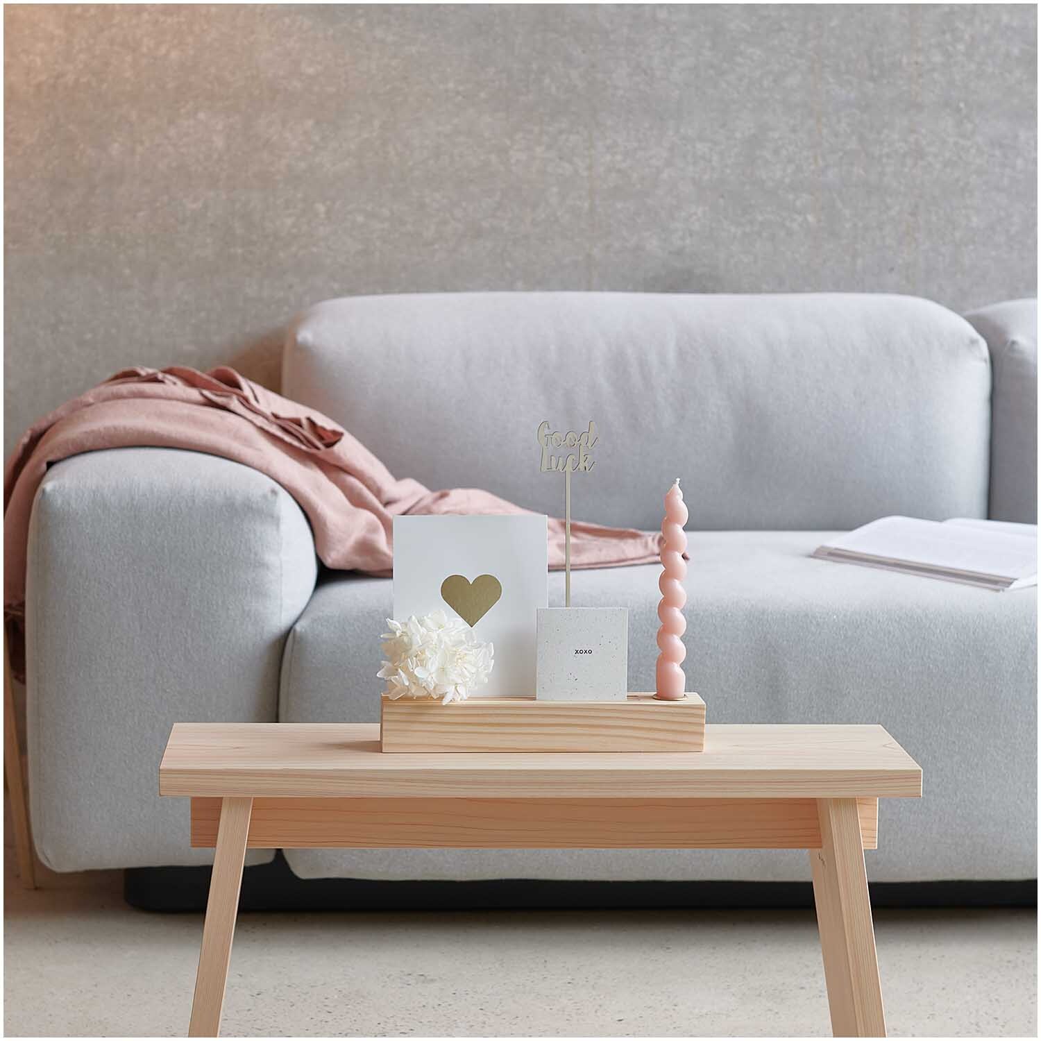 Holzständer für Metallringe & Karten mit Kerzenhalter auf hellem Tisch vor grauem Sofa.