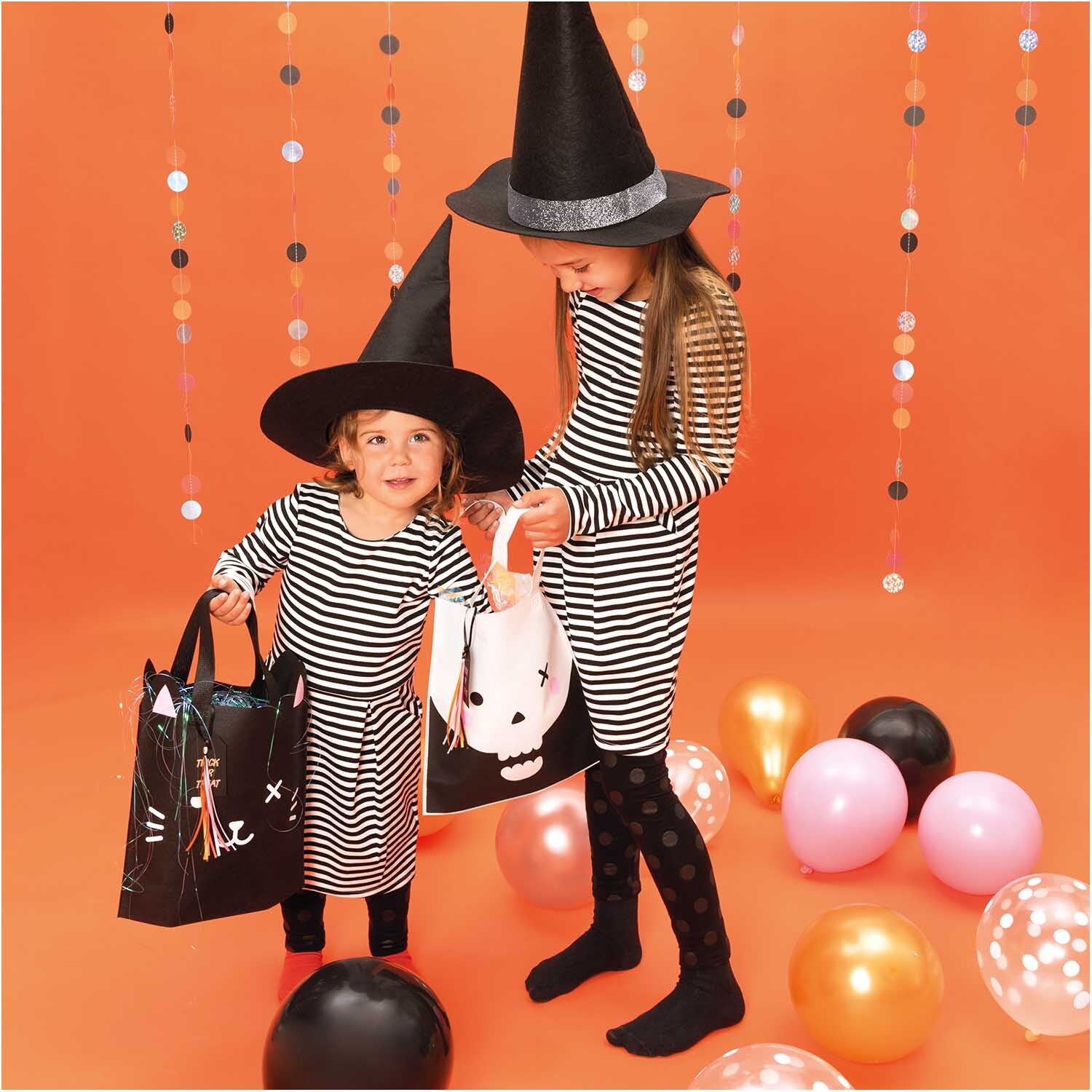 Luftballon Mix Halloween 30cm 12 Stück von Rico Design Luftballon Mix Halloween 30cm 12 Stück: Zwei Kinder in Hexenkostümen mit gestreiften Kleidern und Halloween-Taschen, umgeben von bunten Luftballons.