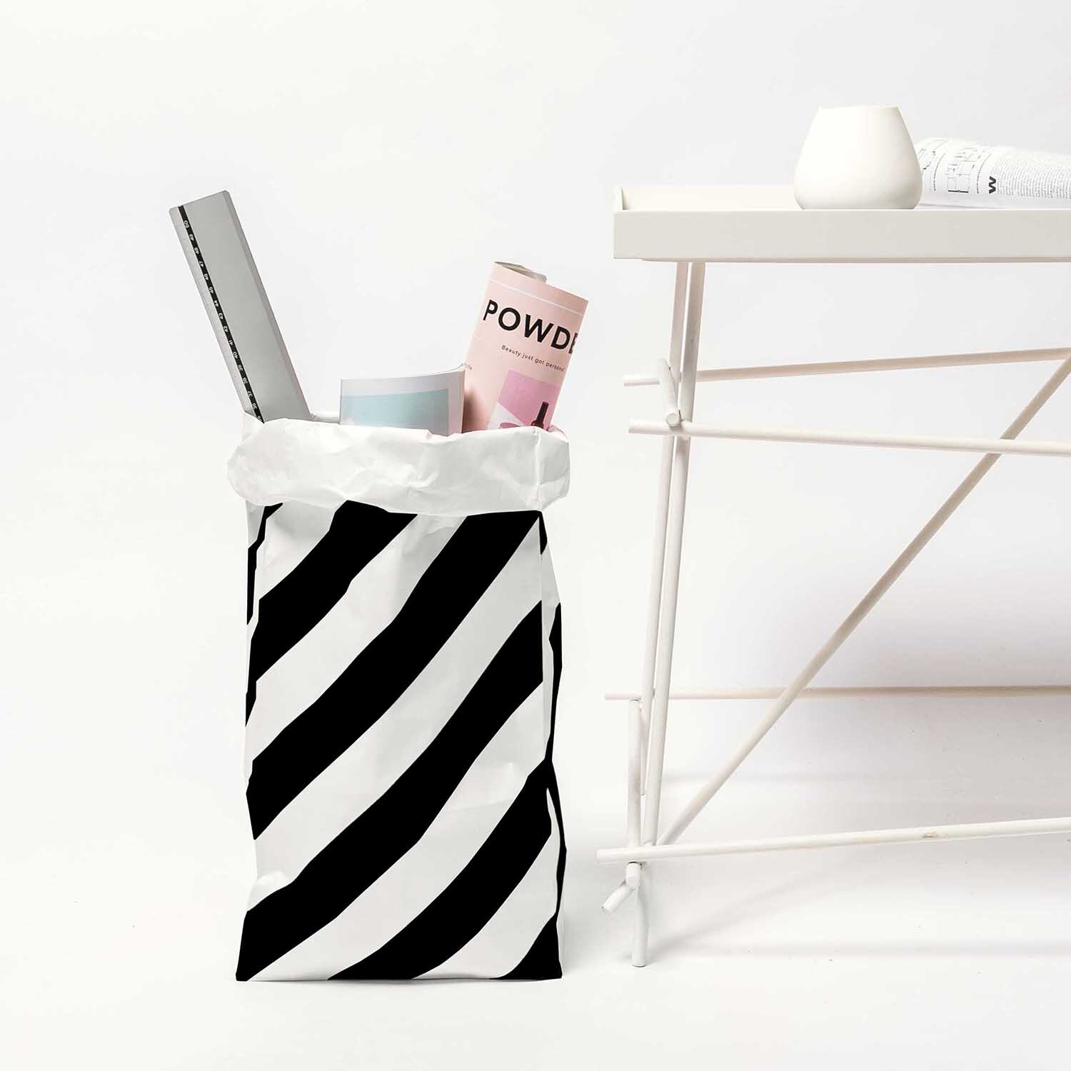 Paper Poetry Maxi-Blockbodenbeutel M Streifen 51x23x13,5cm 2 Stück Farbe Schwarz-Weiß von Rico Design Paper Poetry Maxi-Blockbodenbeutel M mit Streifen, gefüllt mit Magazinen, neben weißem Tisch.
