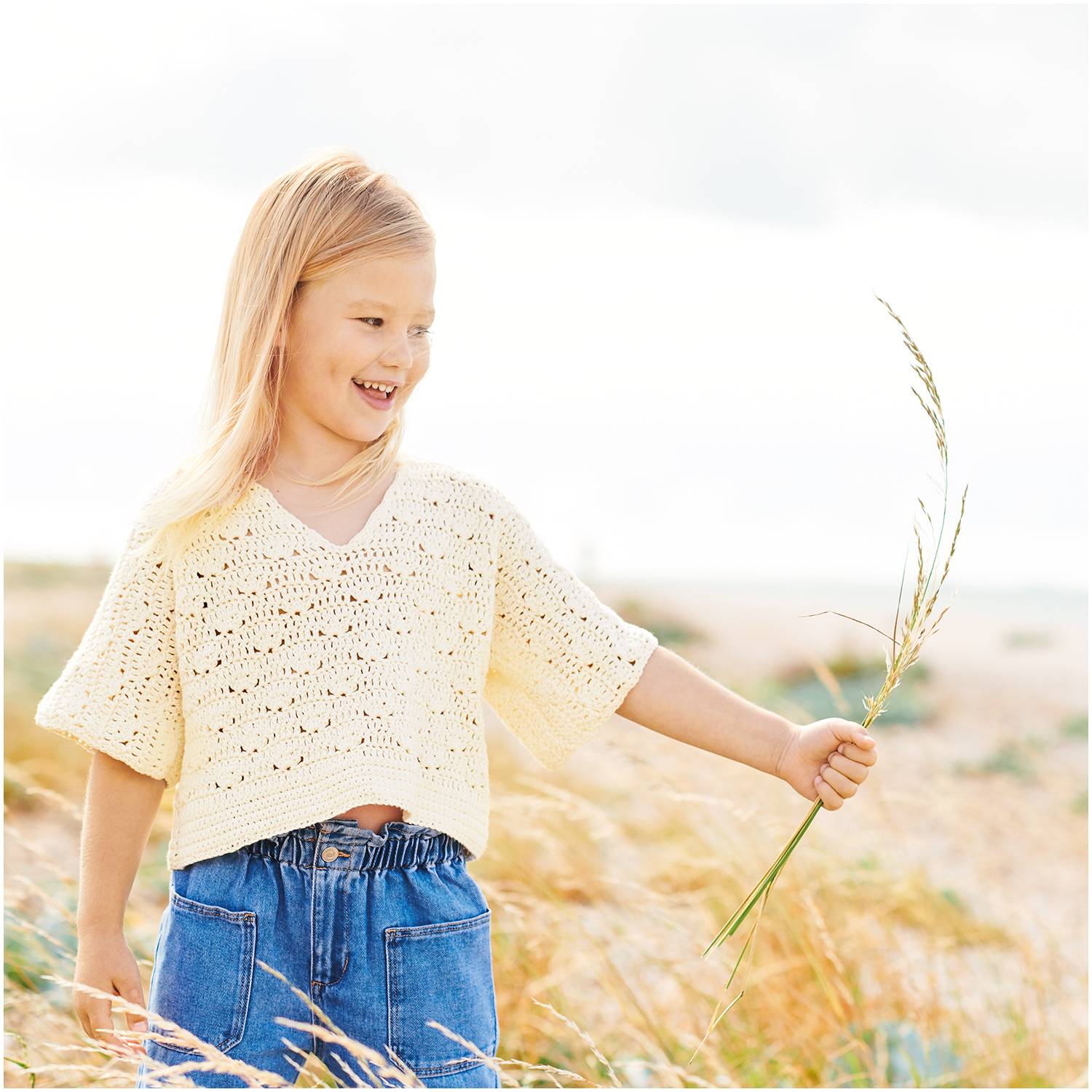 Essentials Organic Cotton dk 50g 105m Couleur Crème from Rico Design Essentials Organic Cotton dk: Mädchen in cremefarbenem Strickpullover von Rico Design auf Wiese.