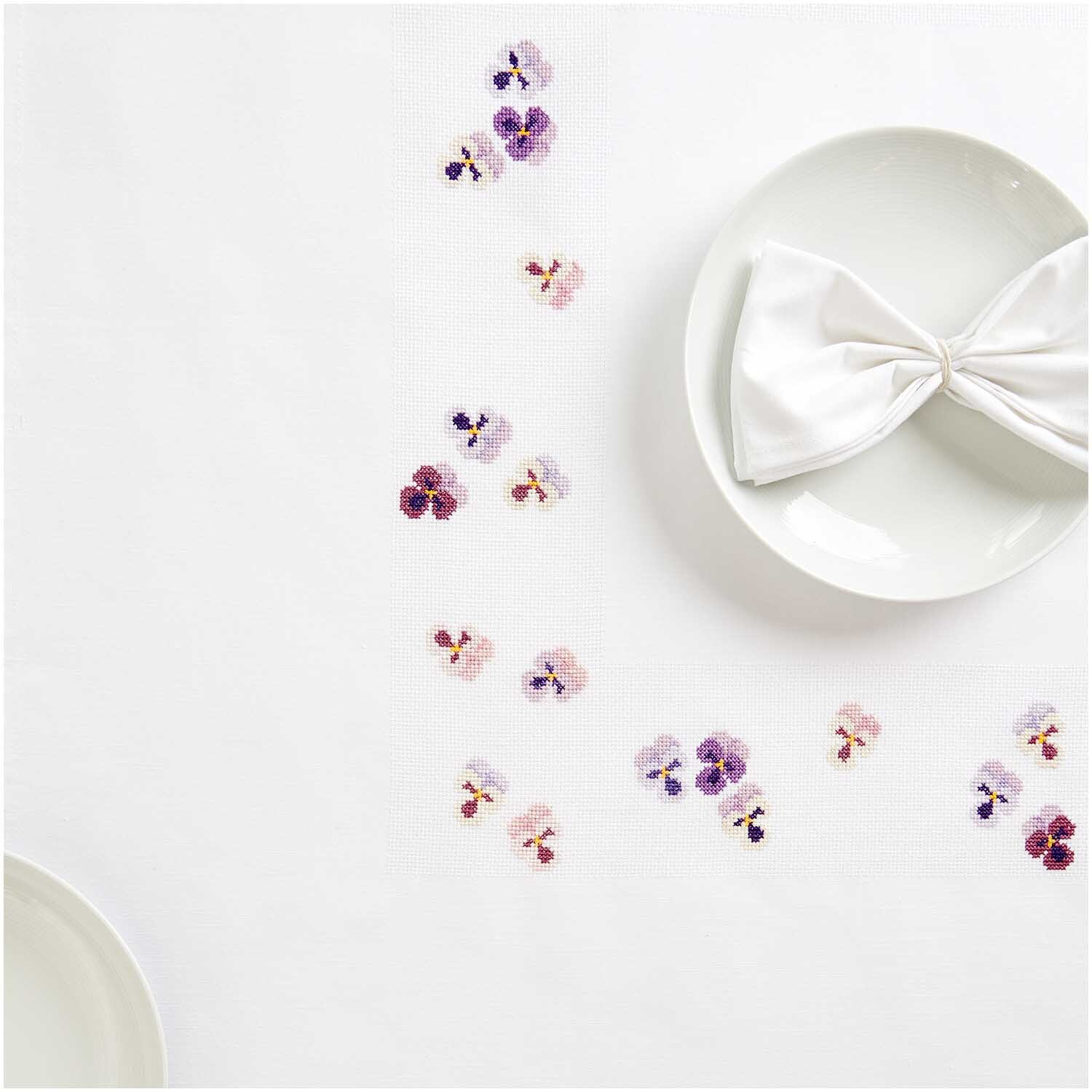 Paquet à broder Nappe Pensées 90x90cm from Rico Design Stickpackung Tischdecke Stiefmütterchen von Rico Design zeigt zarte Blumenstickereien auf weißem Stoff, ideal für elegante Tischdekorationen.