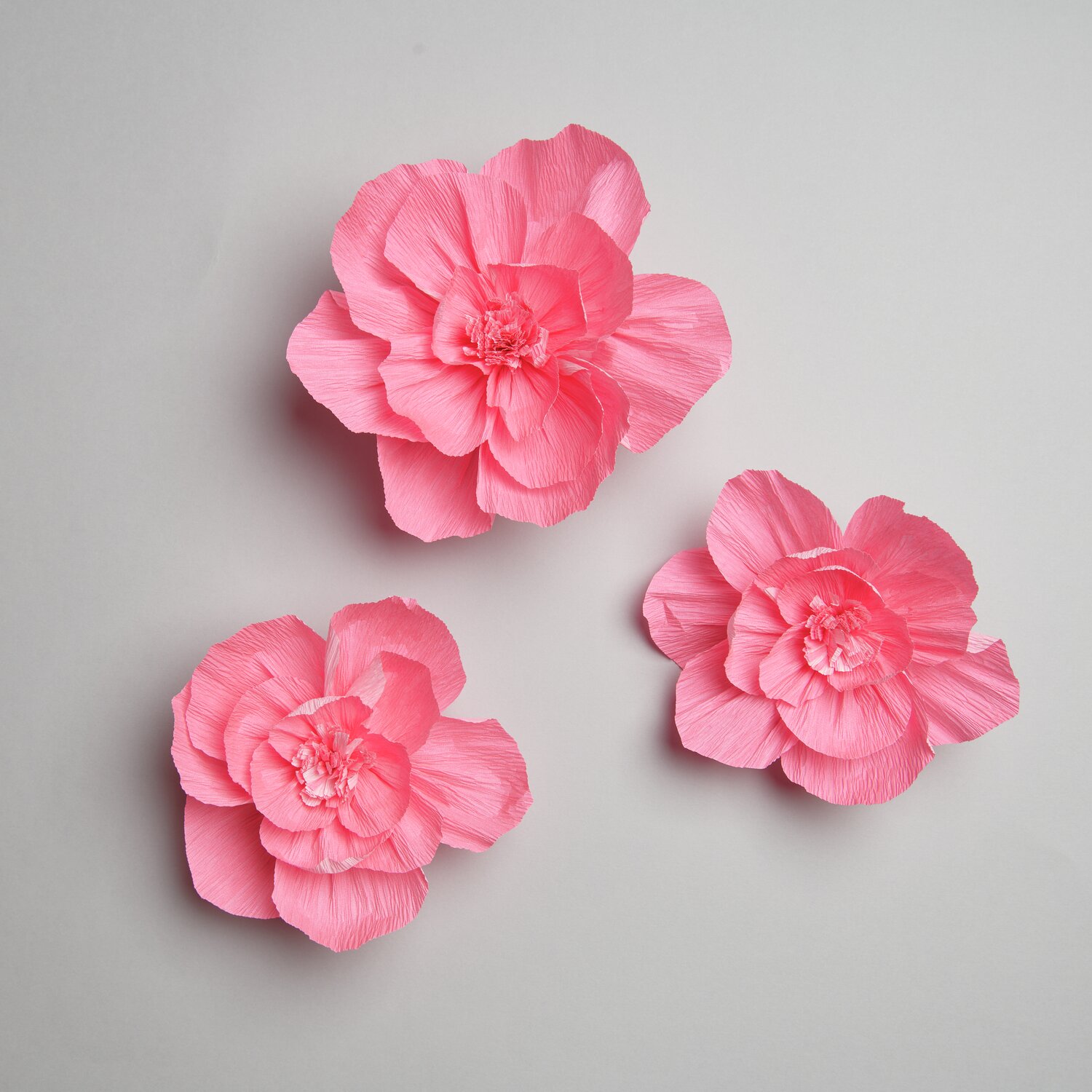 Krepppapier Blüten: Drei kunstvoll gestaltete Blüten in leuchtendem Neonpink von Rico Design.