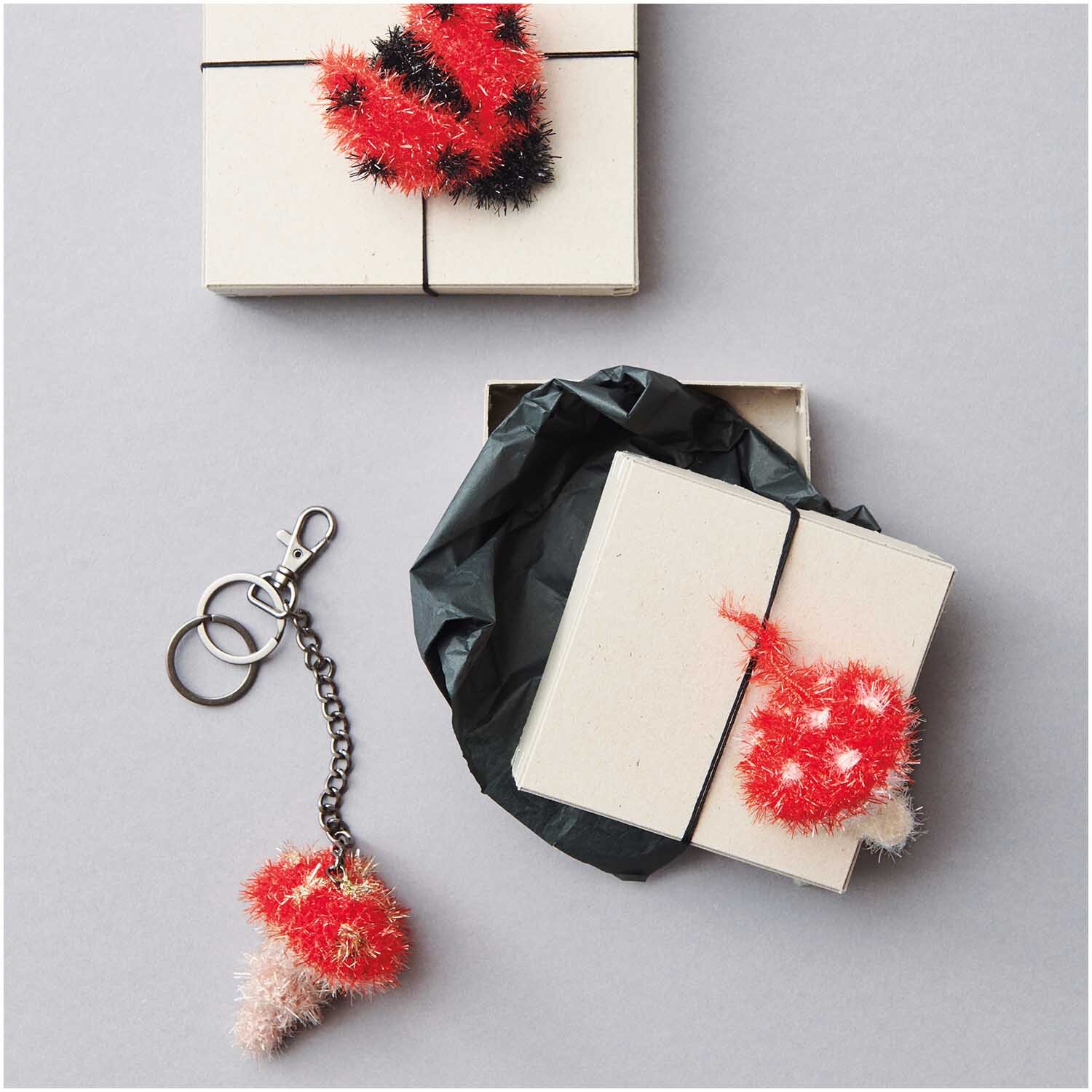 Creative Bubble Set Good Luck! 10x50g von Rico Design Creative Bubble Set Good Luck! von Rico Design mit roten und schwarzen Strickaccessoires, Geschenkbox und Schlüsselanhänger.