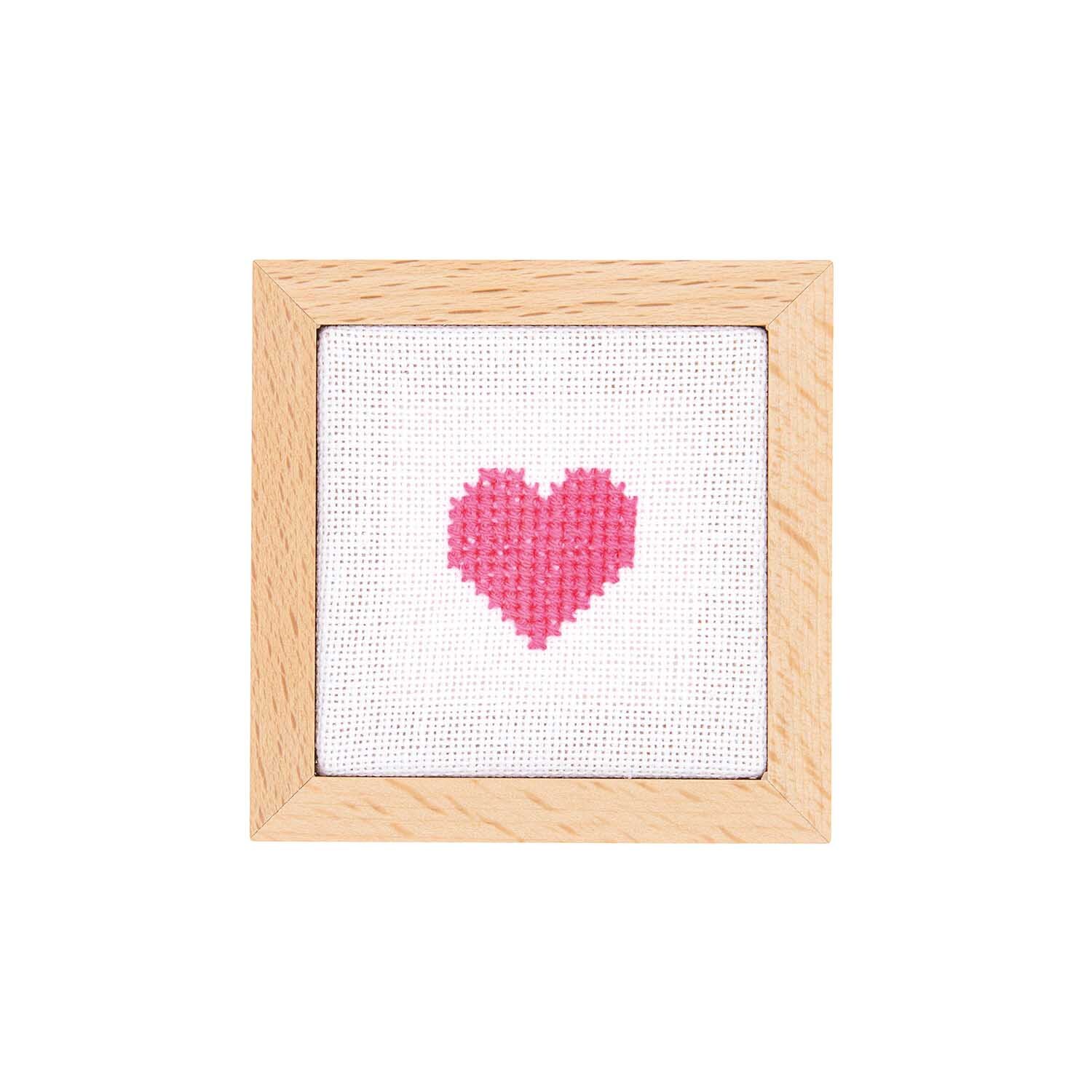Cadre décoratif carré Taille 7x7cm from Rico Design Dekorahmen quadratisch von Rico Design mit rosa Herzstickerei auf weißem Hintergrund, umrahmt von hellem Holz.