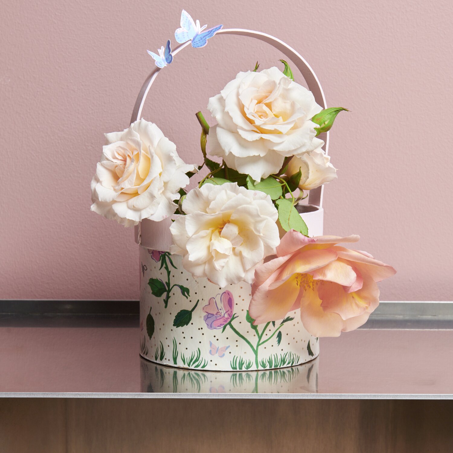 Paper Patch Papier Frühlingswiese: Ein dekorativer Eimer mit Rosen und Schmetterlingen vor rosa Wand.