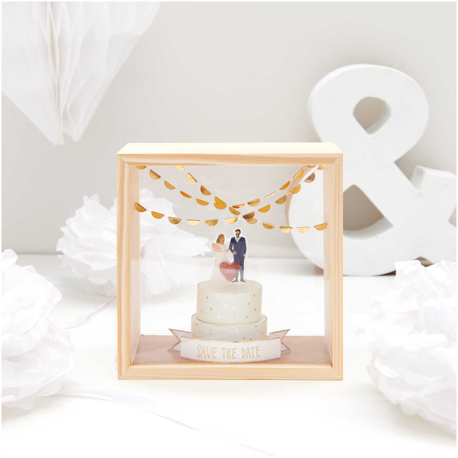 Figurico Objektkasten mit 2 Acrylscheiben Größe 13x13x8cm von Rico Design Figurico Objektkasten mit 2 Acrylscheiben zeigt Hochzeitspaar auf Torte, umgeben von goldenen Girlanden.