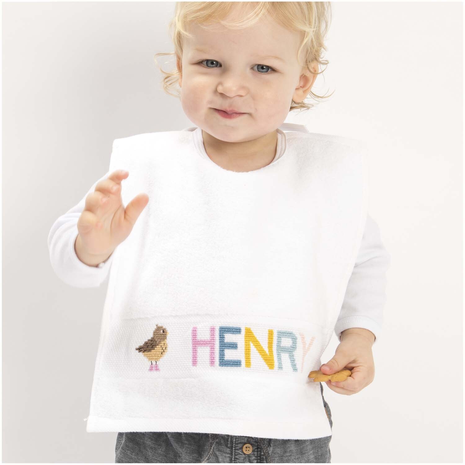 Stickpackung Lätzchen Tiere & Alphabet: Kind trägt weißes Lätzchen mit buntem Alphabet-Design von Rico Design.