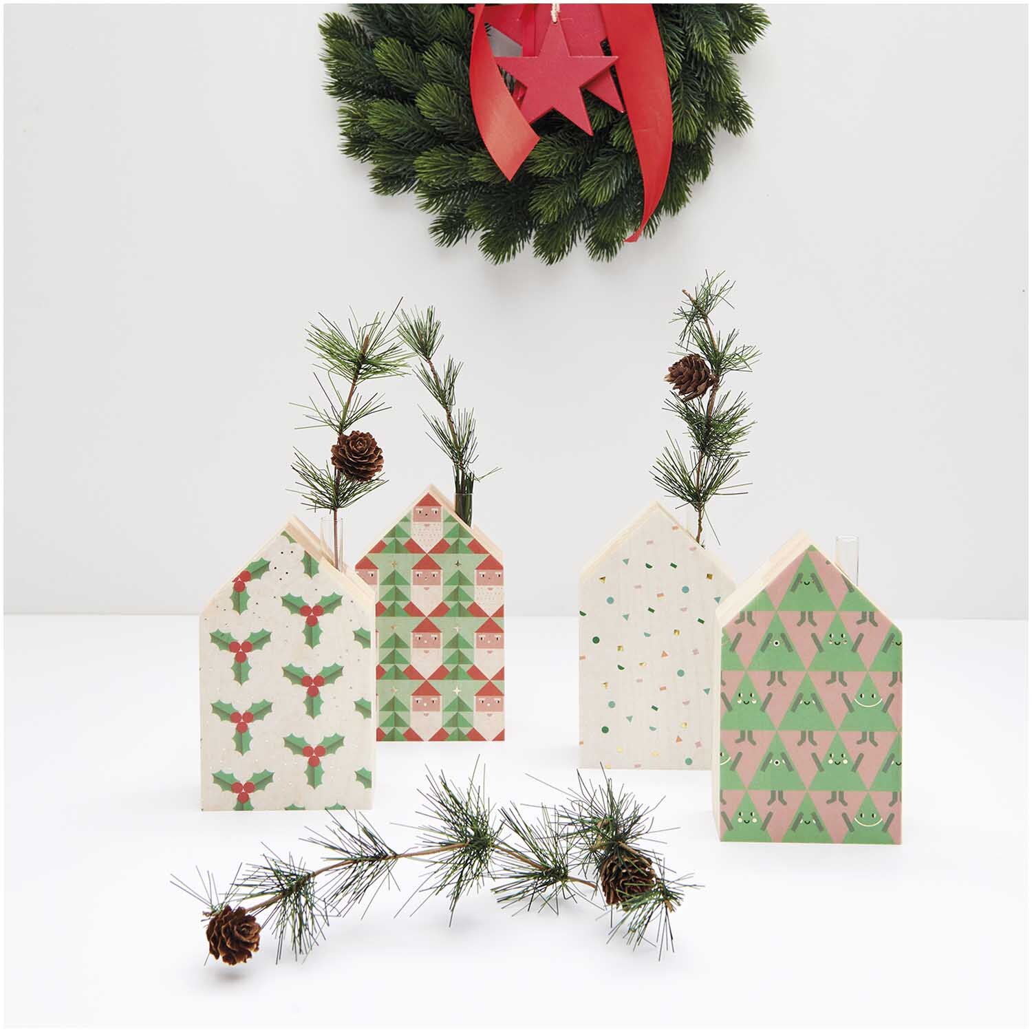 Paper Poetry Paper Patch Papier Weihnachtsmann 30x42cm zeigt festliche Papierhäuser mit Tannenzweigen und einem Kranz im Hintergrund.