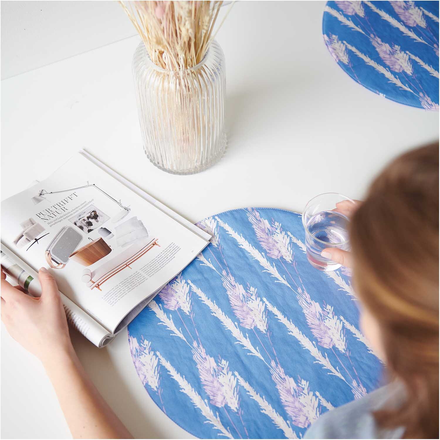 Meterware Druckstoff Pampasgras azur von Rico Design Meterware Druckstoff Pampasgras azur: Tischset mit Pampasgras-Muster in Blau, neben Vase und Magazin.