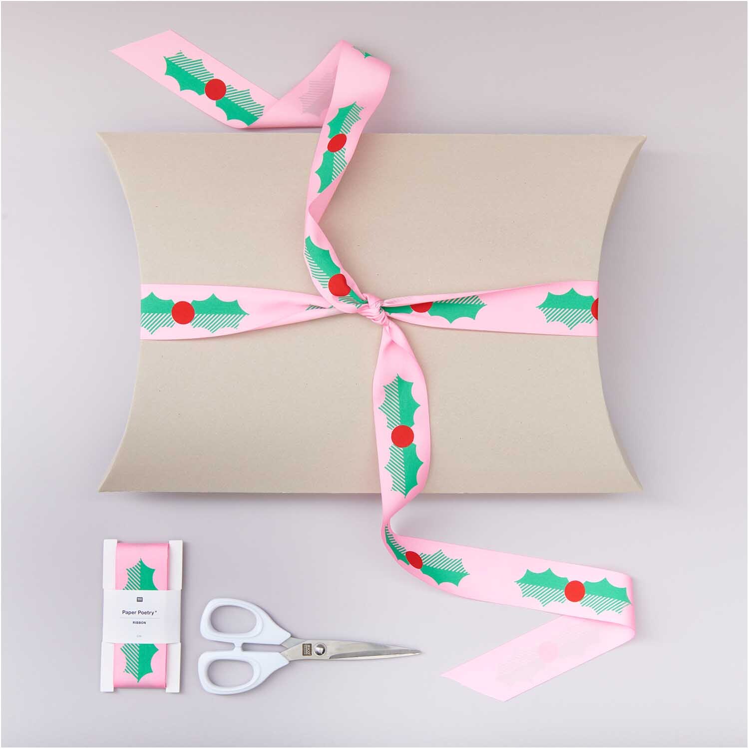 Paper Poetry Taftband Ilex 38mm 3m von Rico Design Paper Poetry Taftband Ilex 38mm 3m, rosa Geschenkband mit grünen Blättern und roten Beeren, dekoriert auf einer Geschenkbox.