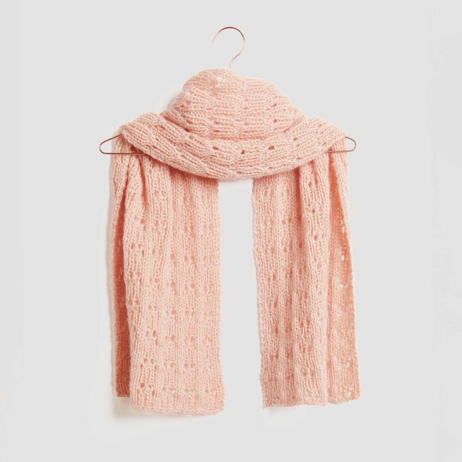 Luxury Merino Alpaca Dream aran 50g 125m Farbe Apricot von Rico Design Ein weicher, rosa Strickschal hängt auf einem Kleiderbügel. Der Schal ist von der Marke Modell Legeware und besticht durch sein elegantes Design. Perfekt für kühle Tage.