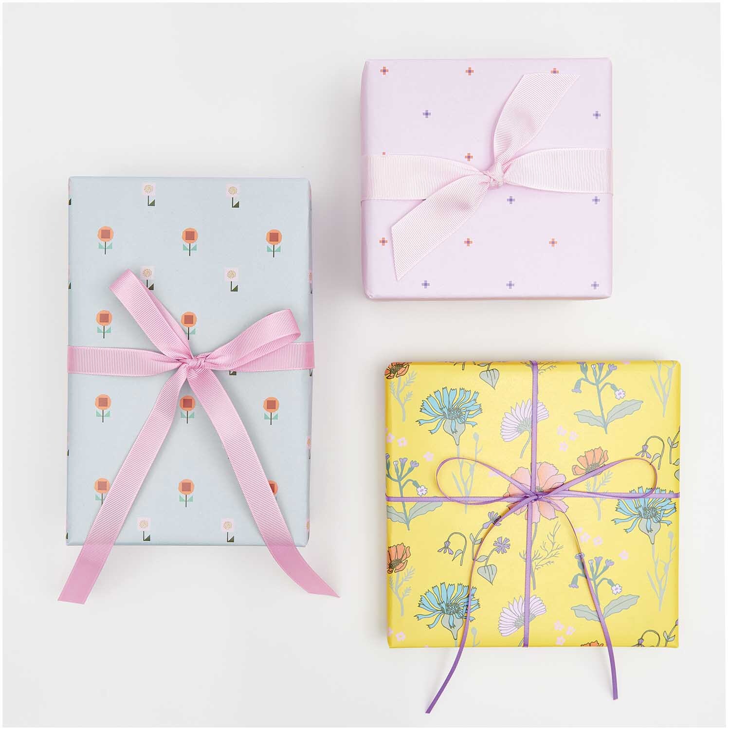 Geschenkpapier Blumen Blau 70cm 2m 80g/m² von Rico Design Geschenkpapier Blumen Rosa: Drei Geschenke in rosa, blau und gelb mit floralen Mustern und Schleifen.