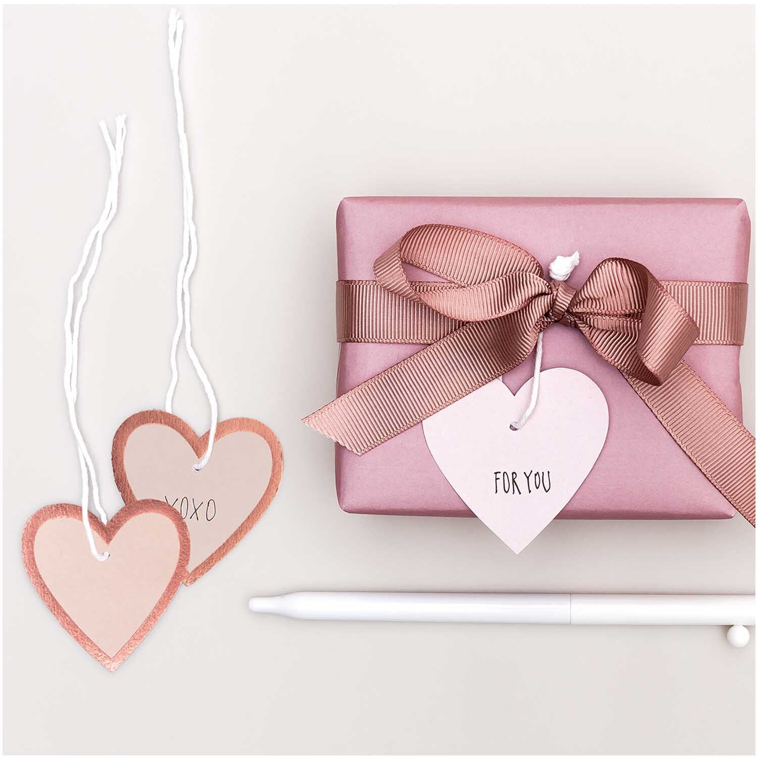Paper Poetry Papieranhänger Herzen M 24 Stück Farbe Puder-Roségold von Rico Design Paper Poetry Papieranhänger Herzen M 24 Stück in Puder-Roségold neben Geschenk mit Schleife.