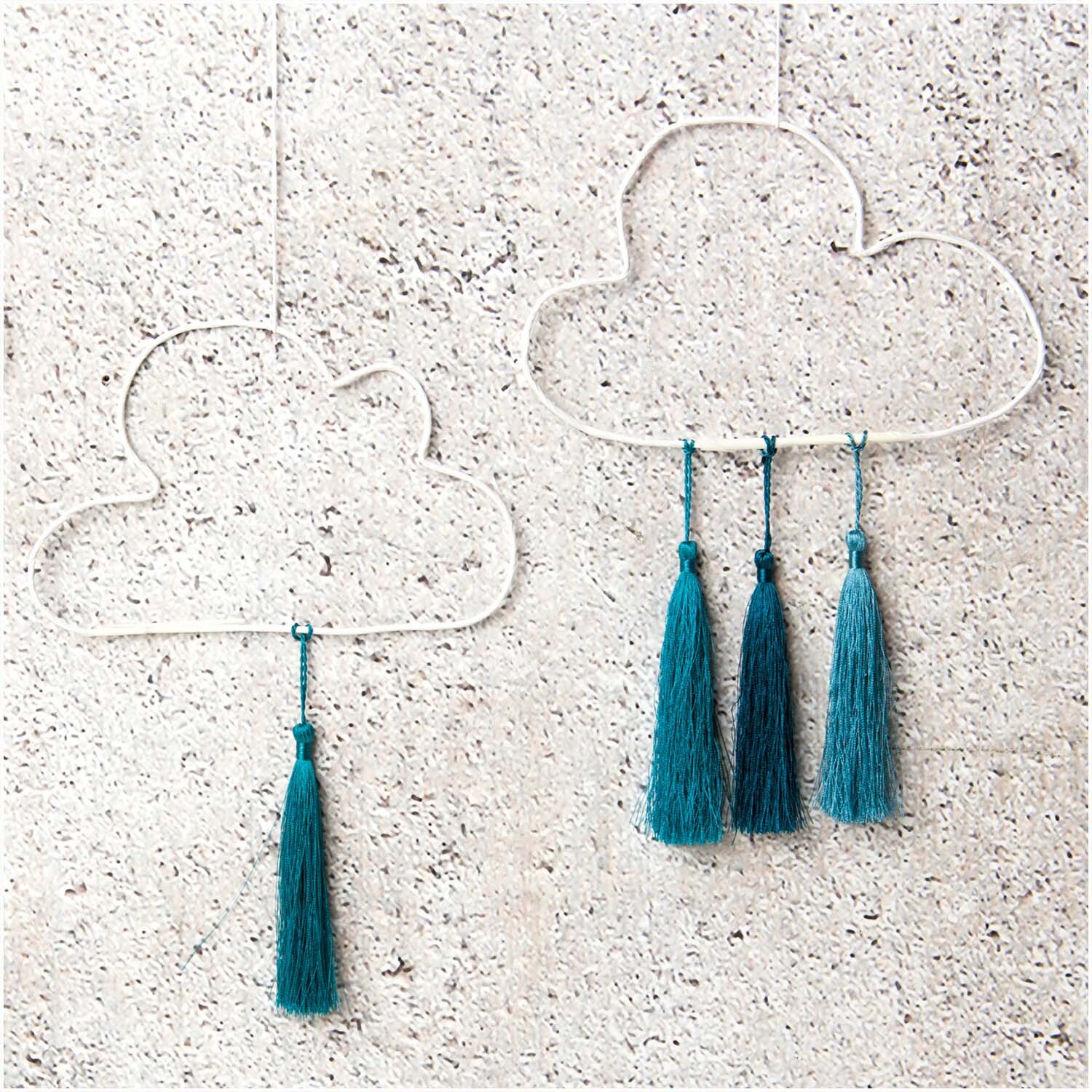 Quasten fein 9cm 5 Stück Farbe Aqua von Rico Design Quasten fein 9cm 5 Stück: Zwei Wolken-Dekorationen mit aqua Quasten an einer Steinwand.