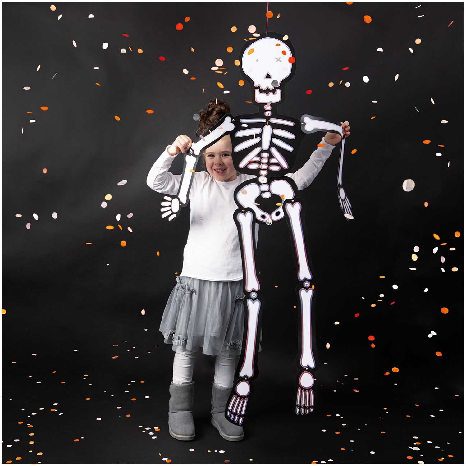 Paper Poetry Hänge-Skelett groß 32x140cm von Rico Design Paper Poetry Hänge-Skelett groß 32x140cm von Rico Design: Kind hält ein großes Skelett vor schwarzem Hintergrund mit bunten Konfetti.