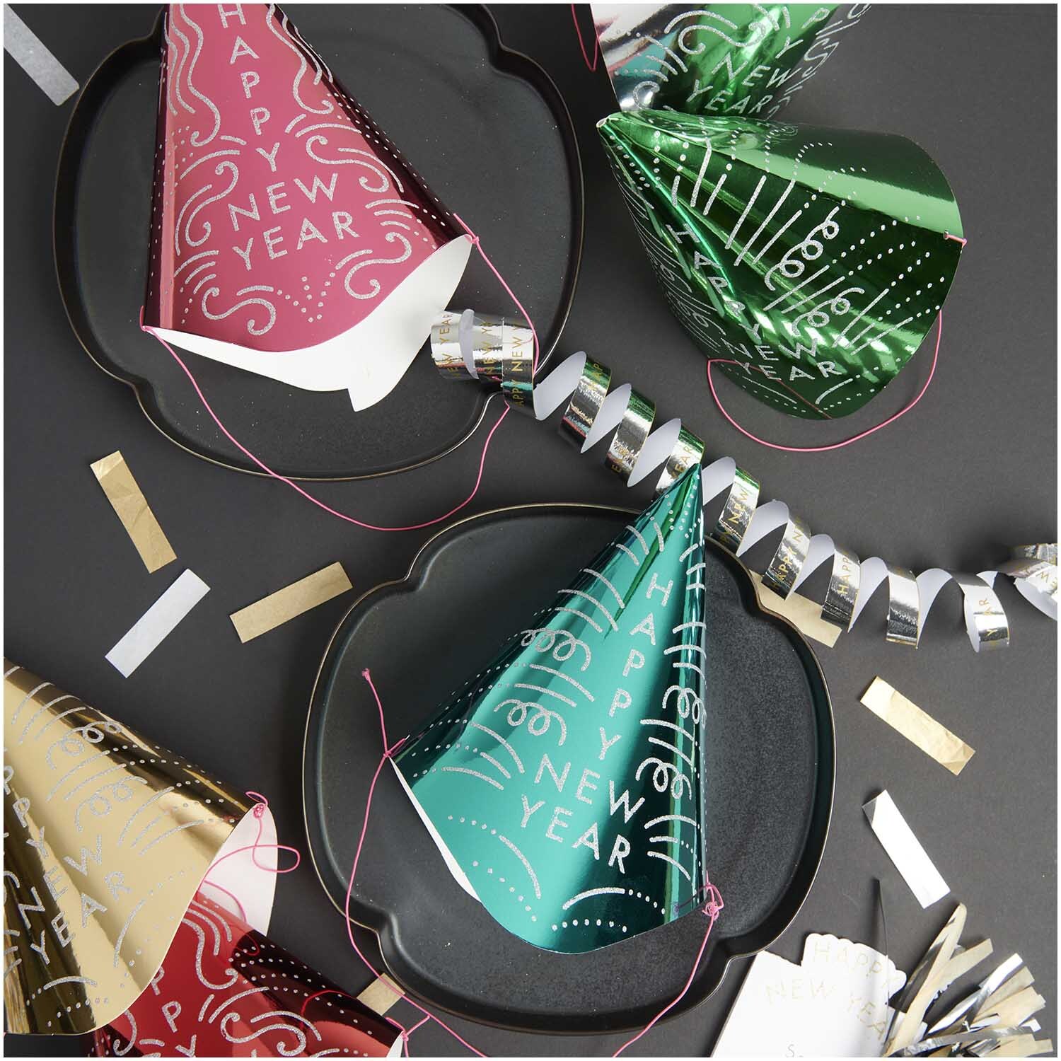 Paper Poetry Partyhüte Happy New Year silber/gold 15x24cm 6 Stück von Rico Design Paper Poetry Partyhüte in verschiedenen Farben auf einem Tisch mit Dekorationen für Silvester.
