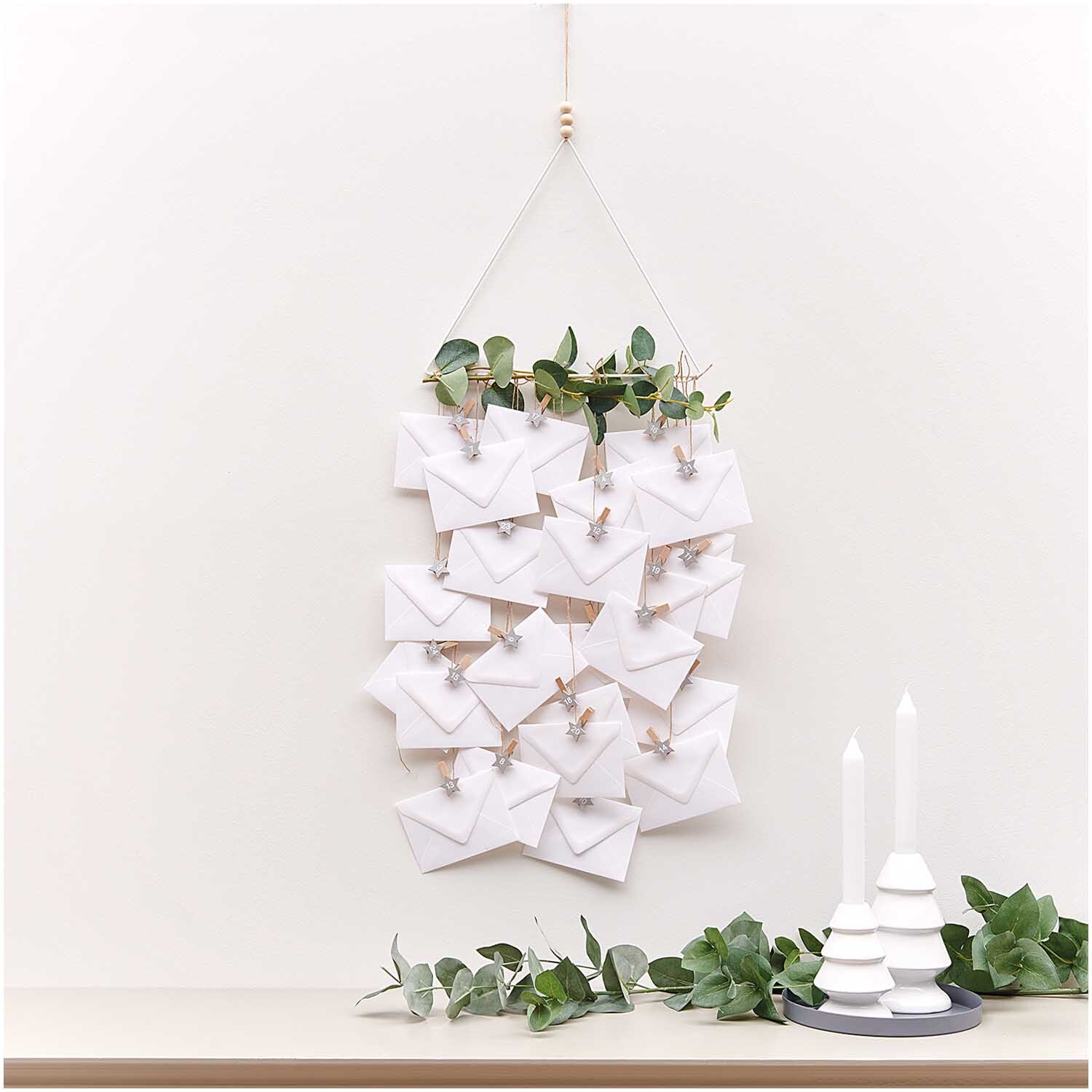 Holzclips Adventskalender Sterne 1-24 3,5cm von Rico Design: Ein dekorativer Kalender mit silbernen Clips, aufgehängt an einer Wand mit grünen Zweigen.