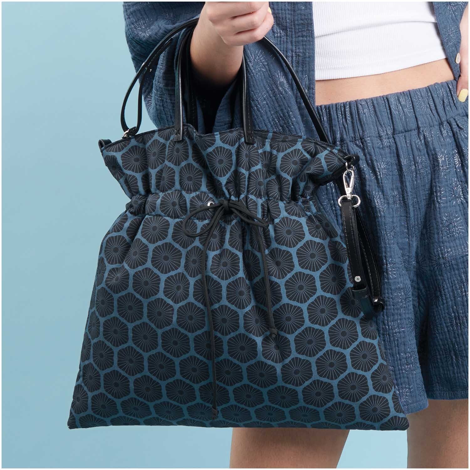 Meterware Baumwoll-Popelin blau Rosette von Rico Design Meterware Baumwoll-Popelin blau Rosette: Frau trägt eine stilvolle Tasche mit blauem Rosettenmuster von Rico Design.