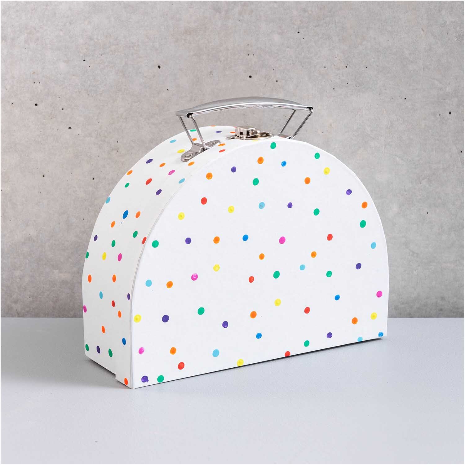 Koffer aus Pappe halbrund weiß Größe 20x15x7cm von Rico Design Koffer aus Pappe halbrund weiß mit bunten Punkten, von Rico Design, auf grauem Hintergrund.