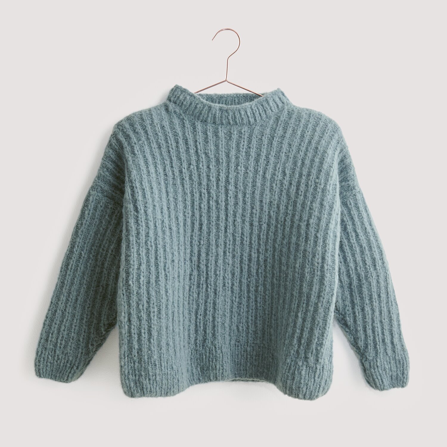 Luxury Pure Baby Alpaca 50g 150m Farbe Rauchblau von Rico Design Strickset Pullover Modell 12 aus Luxury Knits, gestrickt in weichem Blau, präsentiert auf einem Kleiderbügel. Ideal für kühle Tage.
