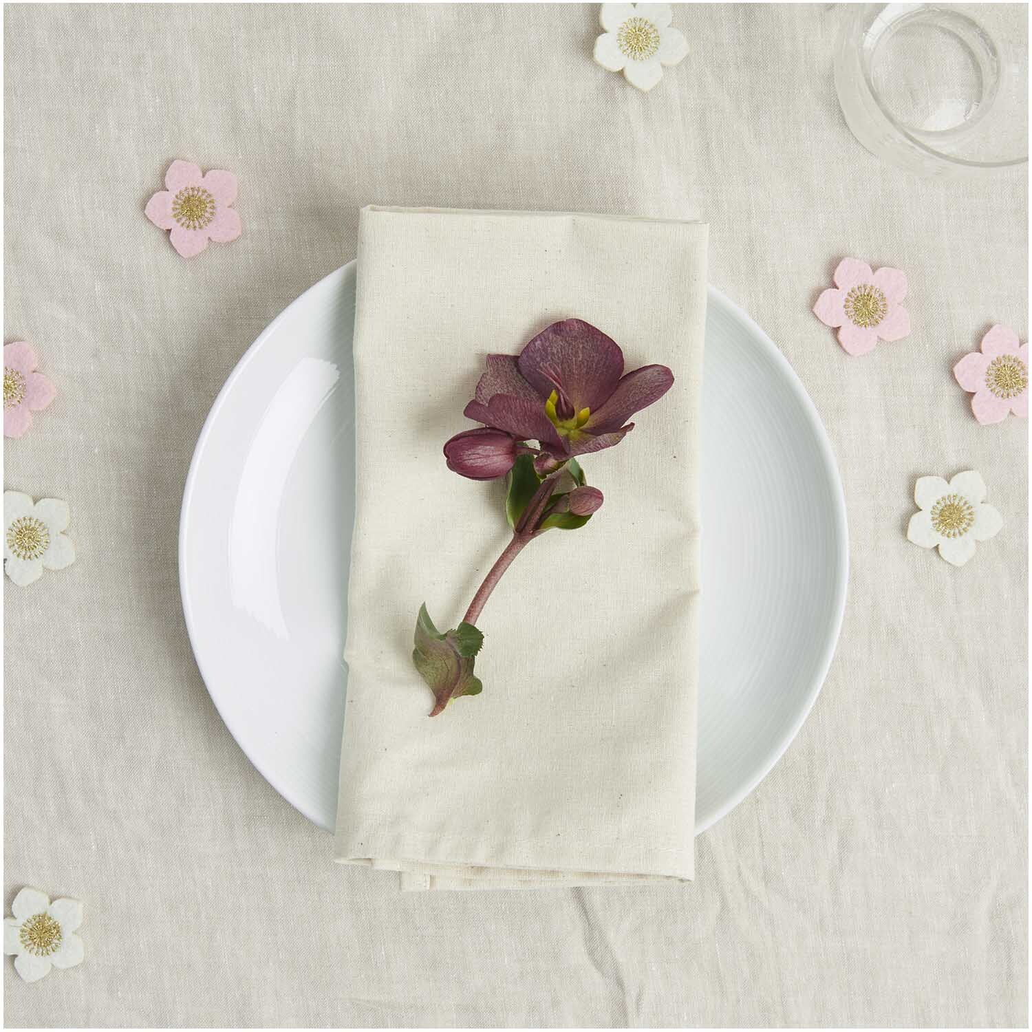 Filzstreu Christrosen bestickt 3,5x3,4cm 8 Stück Farbe Pink-Gold von Rico Design Filzstreu Christrosen bestickt auf einem Teller mit Serviette, umgeben von dekorativen Blüten.