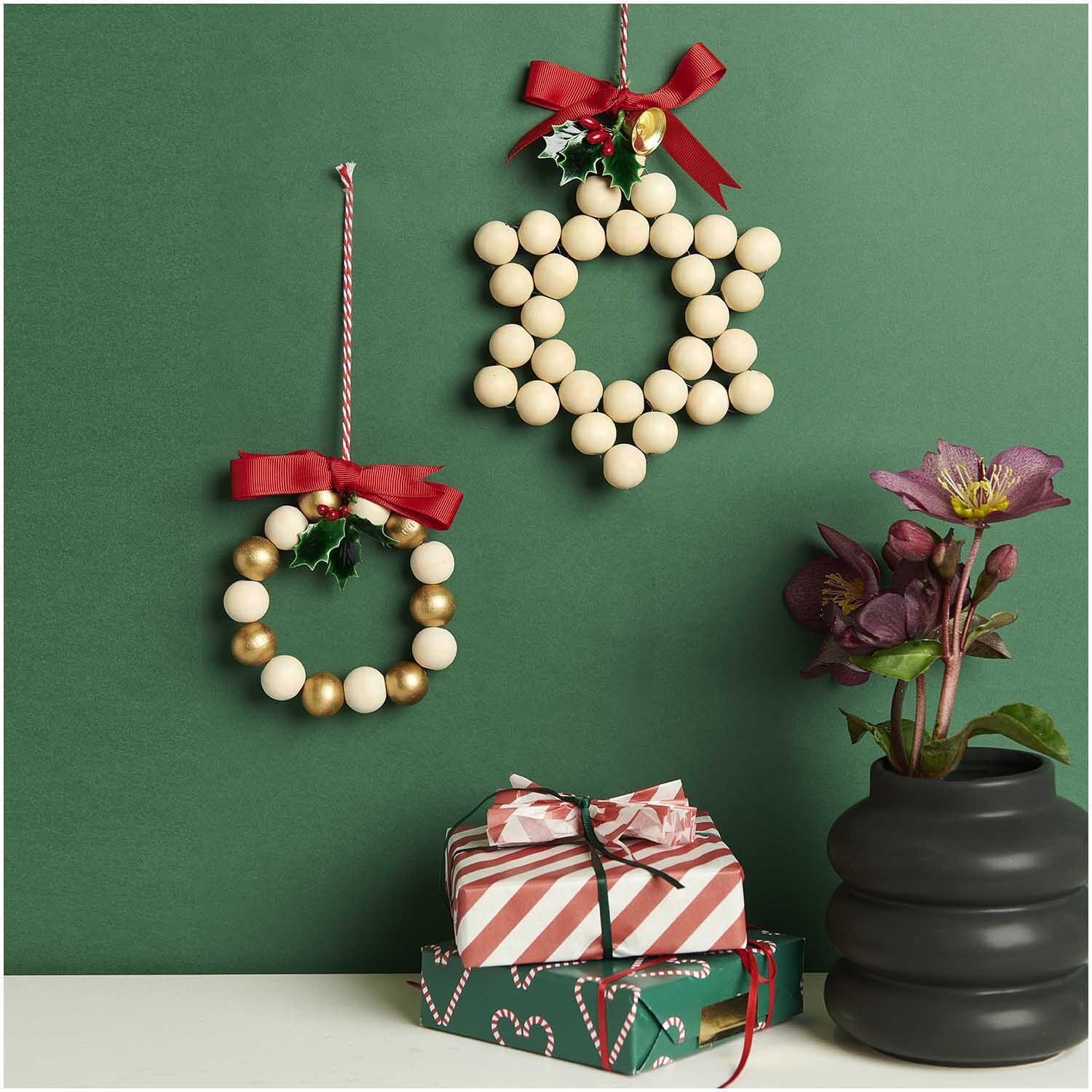 Bastelset Holzperlen Kranz natur-gold 22-teilig von Rico Design Bastelset Holzperlen Kranz natur-gold: Zwei dekorative Kränze aus Holzperlen mit roten Schleifen, neben Geschenken und Blumen. Ideal für festliche Dekorationen.