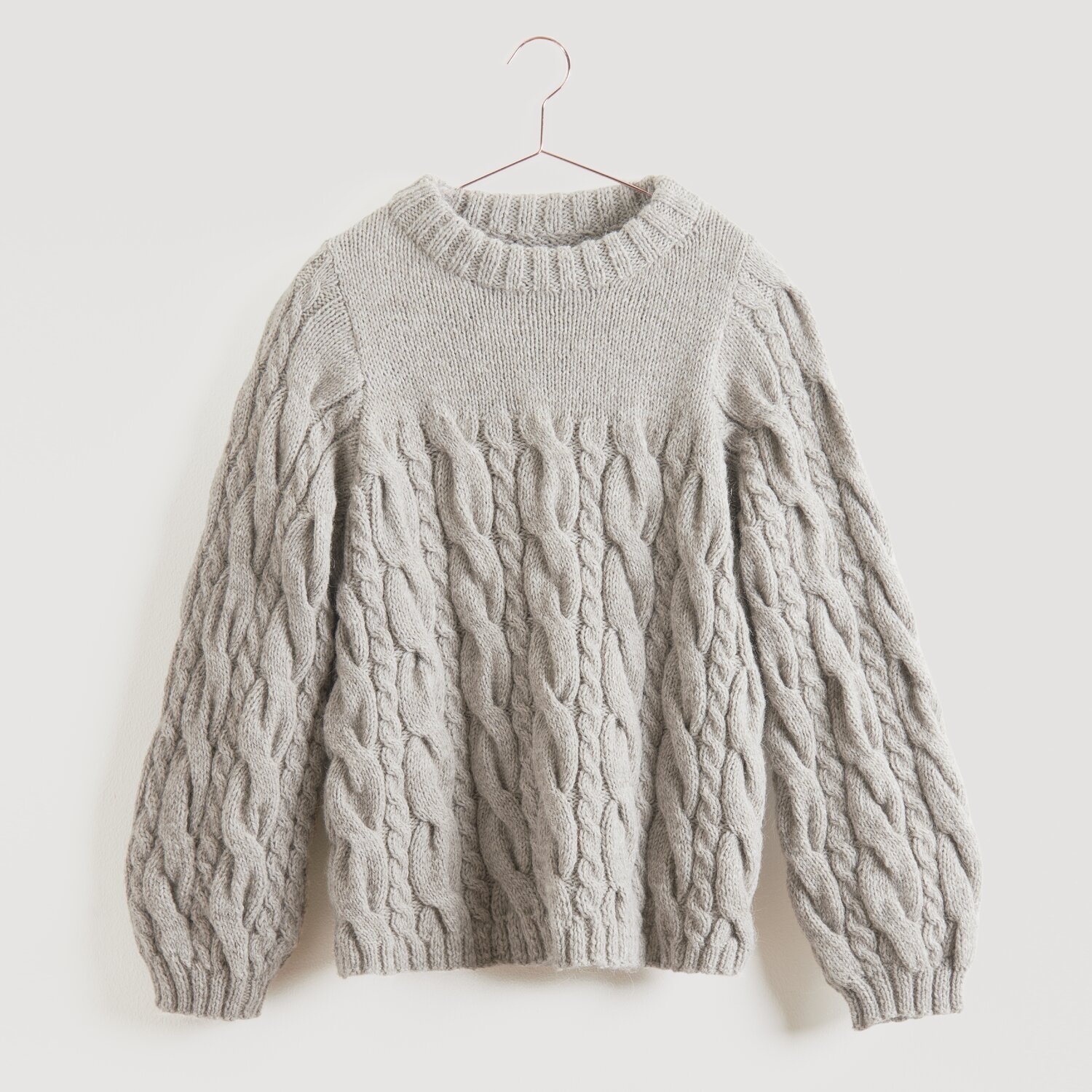 Soft Alpaca 50g 125m Farbe Beige von Rico Design Grauer Strickpullover von Modell Legeware, aufgehängt an einem Kleiderbügel. Der Pullover hat ein Zopfmuster und lange Ärmel, ideal für kühle Tage. Perfekt für einen lässigen, stilvollen Look.