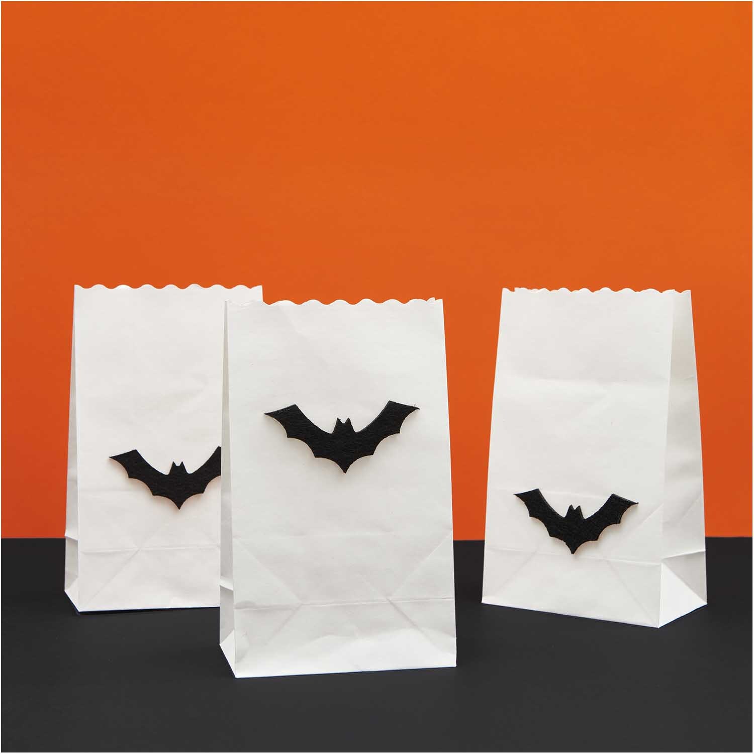Filzstreu Fledermaus schwarz 6 Stück von Rico Design Filzstreu Fledermaus schwarz 6 Stück: Weiße Papiertüten mit schwarzen Fledermausmotiven vor orangefarbenem Hintergrund.