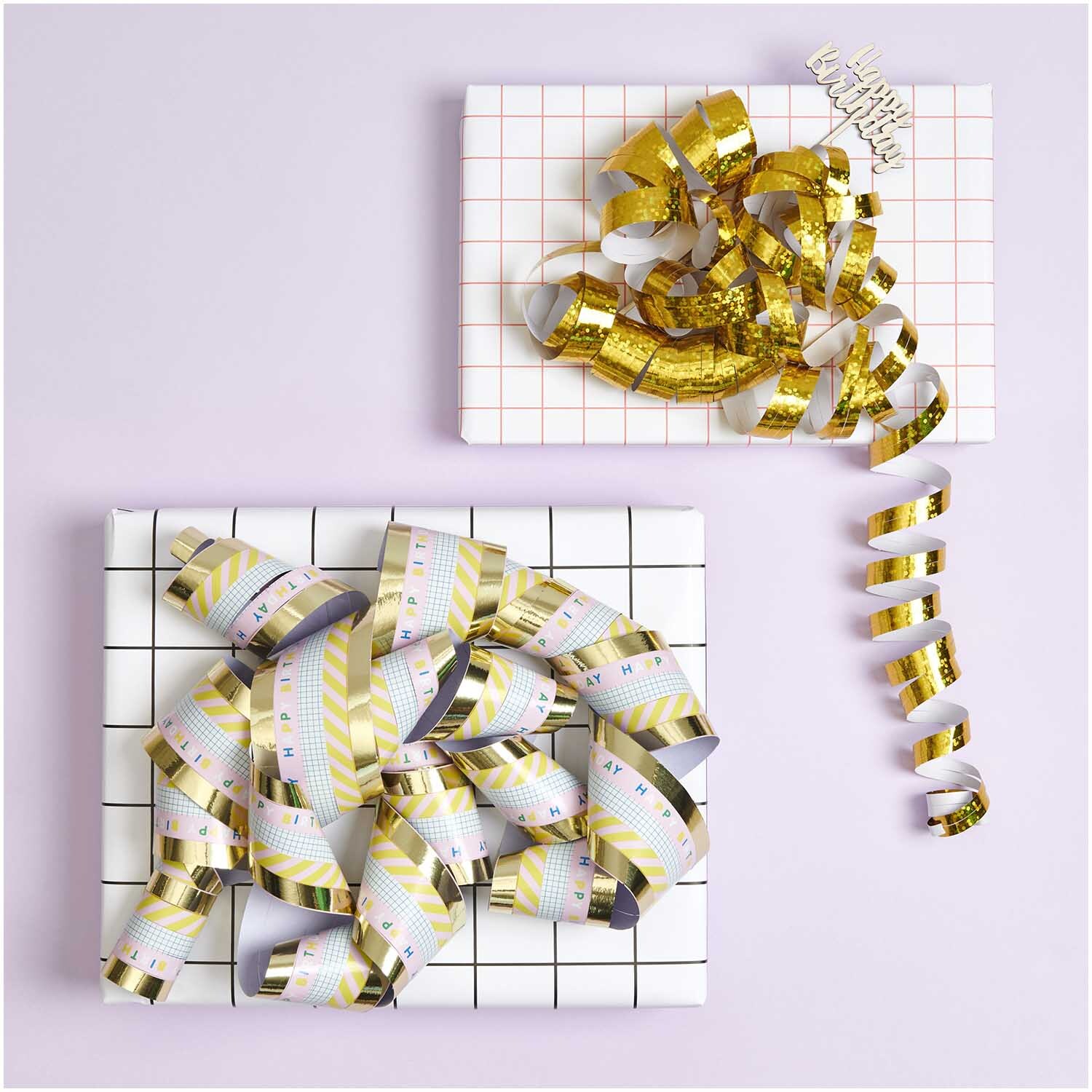 Banderoles Happy Birthday 3,8m from Rico Design Luftschlangen Happy Birthday 3,8m von Rico Design auf Geschenkboxen in Gold und Weiß arrangiert. Ideal für festliche Dekorationen.