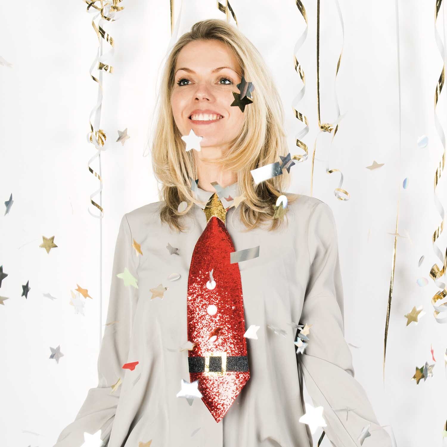 Krawatte Christmas von Rico Design Krawatte Christmas: Eine Frau trägt eine rote, glitzernde Krawatte von Rico Design, umgeben von Sternkonfetti.