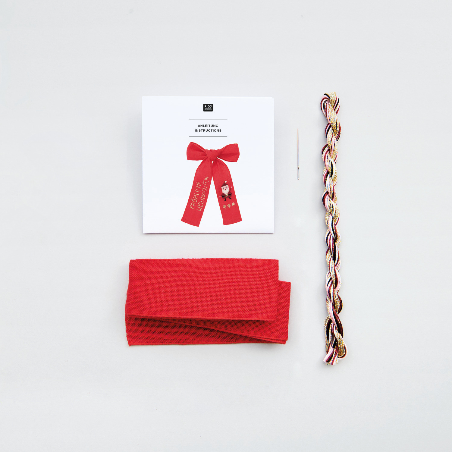 Stickpackung Schleife Nikolaus 12x19cm von Rico Design Stickpackung Schleife Nikolaus von Rico Design mit rotem Stoff, Garn und Nadel auf weißem Hintergrund.