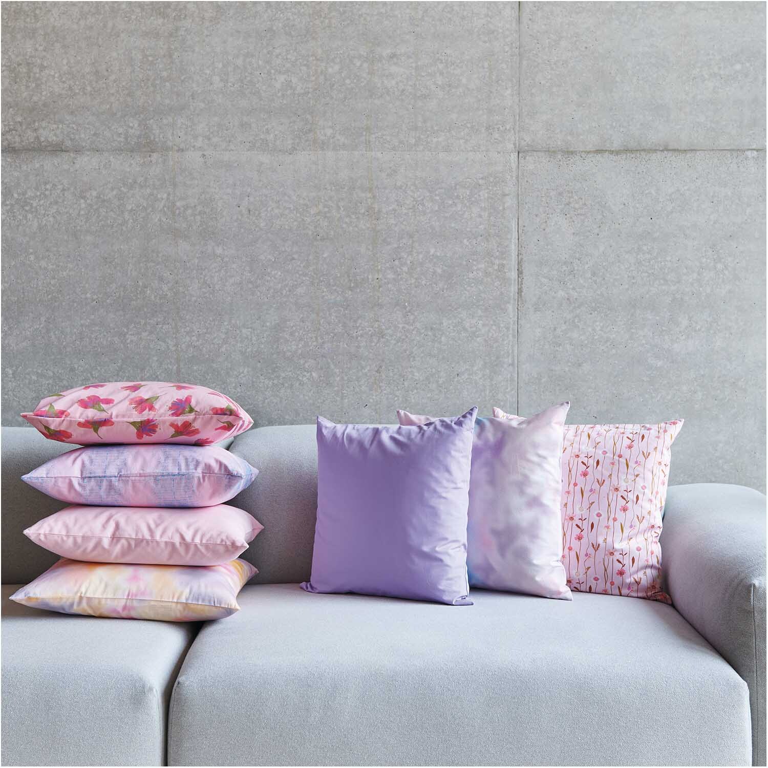 Meterware Druckstoff Muster bonbonrosa-azur von Rico Design Meterware Druckstoff Muster bonbonrosa-azur: Bunte Kissen auf grauem Sofa, ideal für stilvolle Wohnräume.