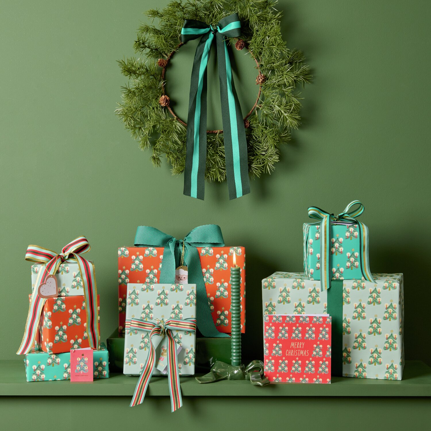 Paper Poetry bande tissée diagonale 50mm 3m Couleur Vert from Rico Design Geschenkverpackungen in verschiedenen Größen, eingewickelt in buntes Paper Poetry Geschenkpapier mit Tannenbaum-Motiven von Rico Design. Farbenfrohe Bänder und eine grüne Kranzdekoration ergänzen das festliche Arrangement.