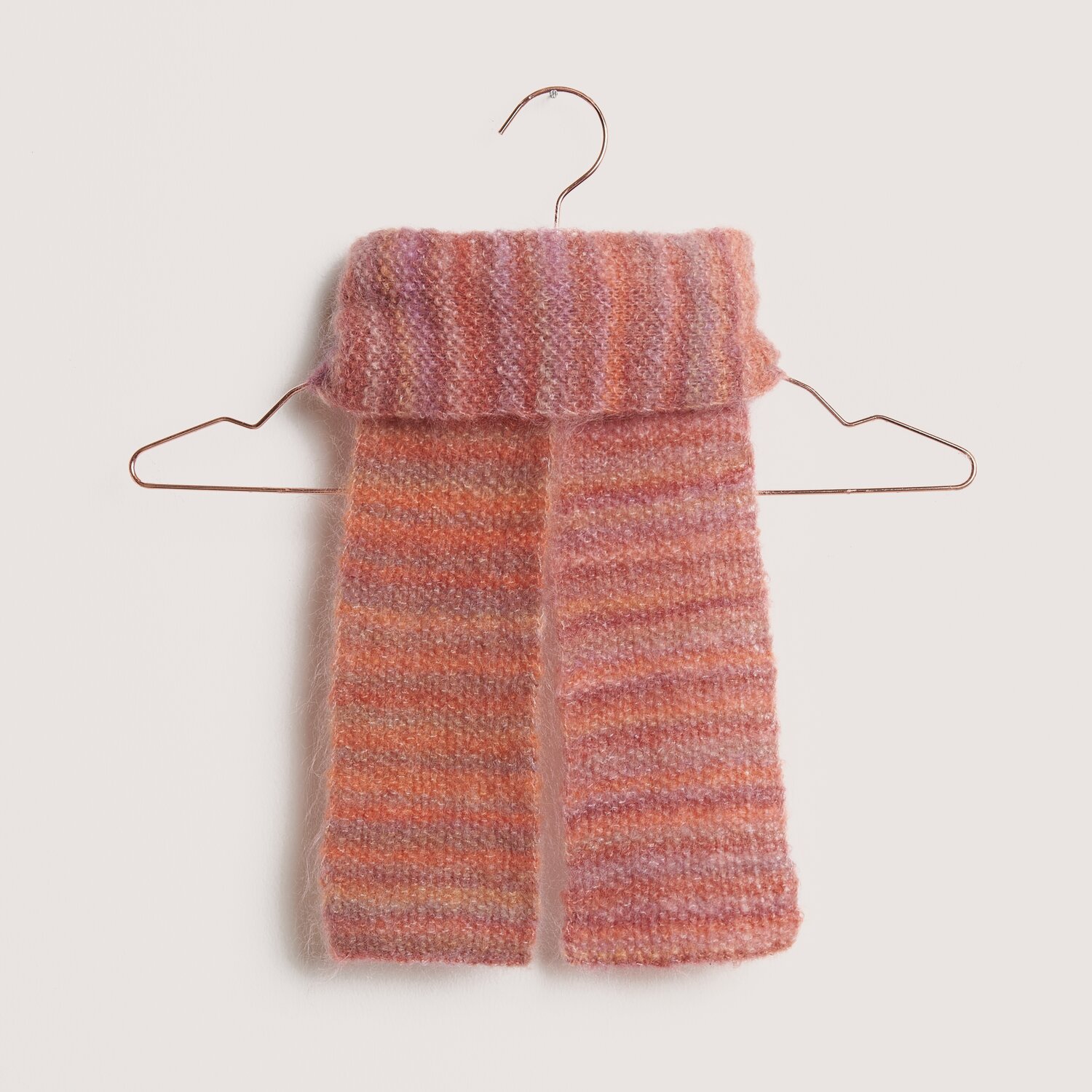 Fashion Meri Mohair Print 50g 275m Couleur Happy Sunrise from Rico Design Fashion Meri Mohair Print Schal in Rosa-Orange auf einem Kleiderbügel, ideal für kühle Tage.