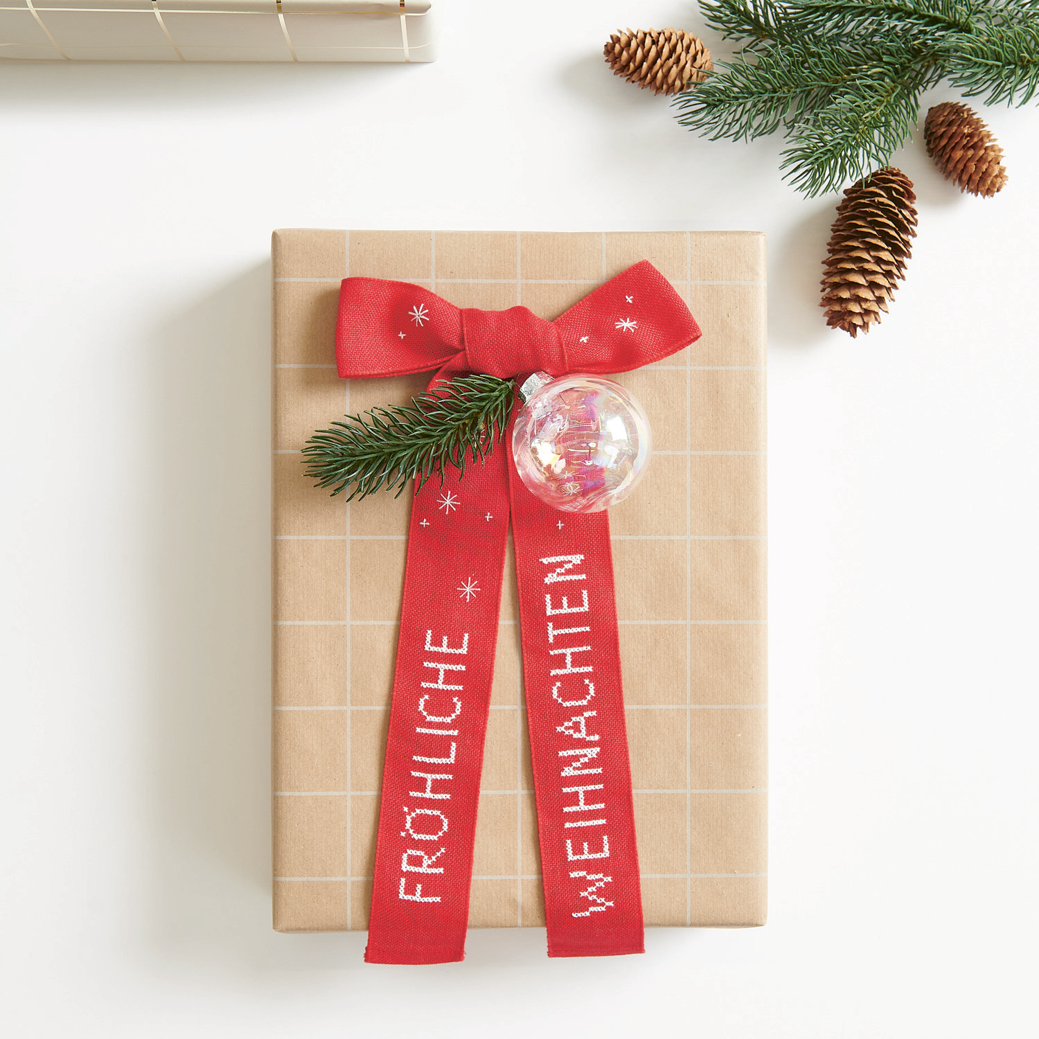 Stickpackung Schleife Fröhliche Weihnachten 16x31cm von Rico Design Stickbuch Put a Bow on It Nr. 185: Geschenk mit roter Schleife und Tannenzweig, verziert mit "Fröhliche Weihnachten".