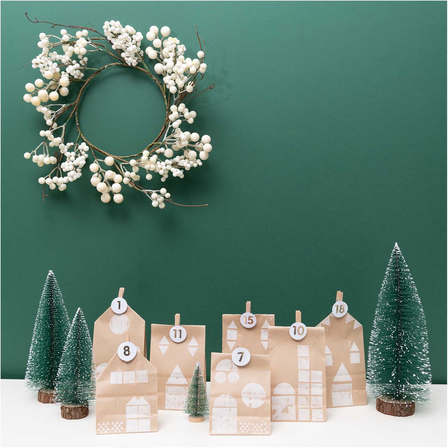Paper Poetry Adventskalenderset mit 24 braunen Tüten, dekoriert mit Tannenbäumen und einem Kranz. Ideal für kreative Weihnachtsdekoration.