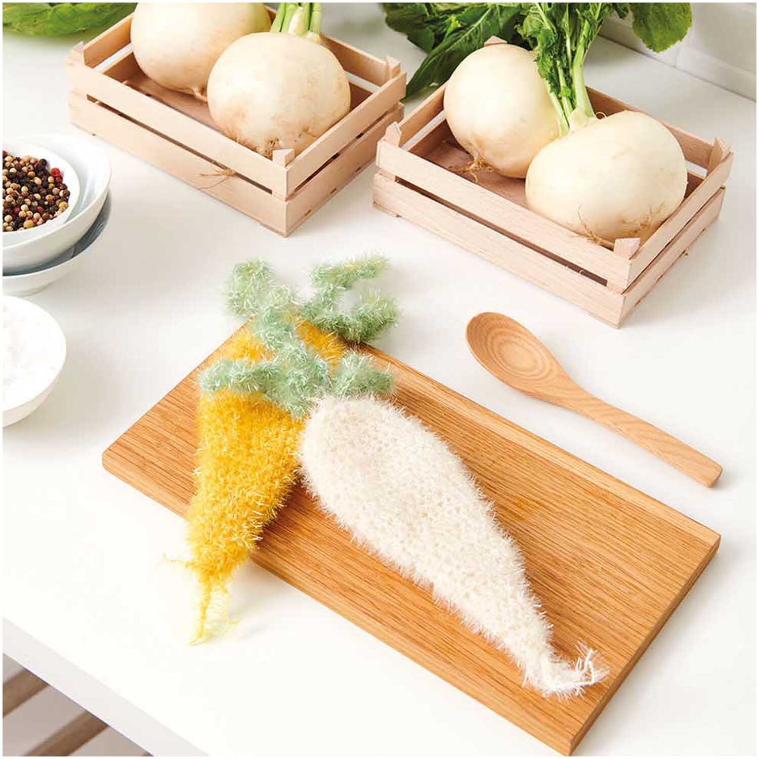 Creative Bubble: Zwei gestrickte Karotten-Schwämme auf einem Holzbrett, umgeben von frischem Gemüse.