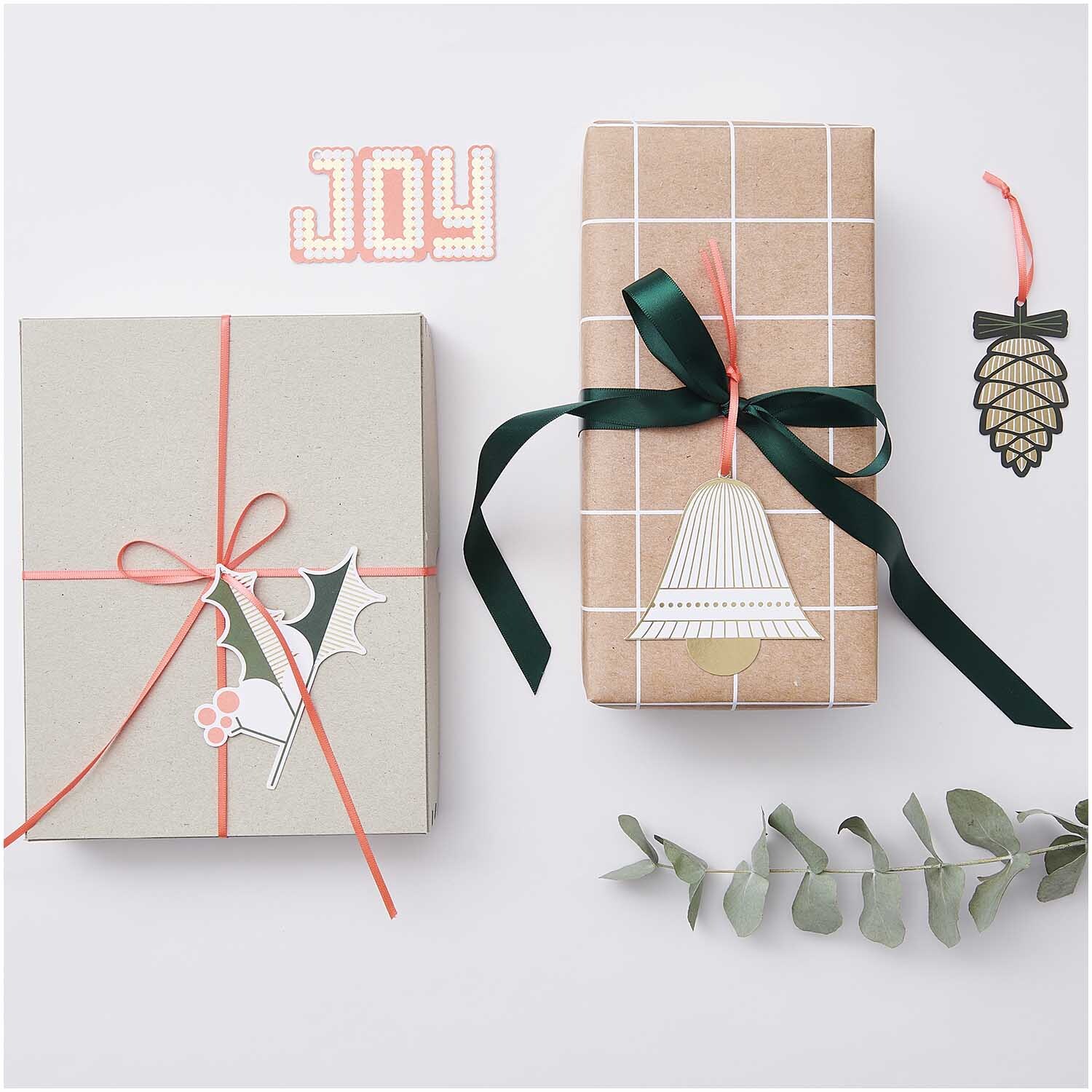 Paper Poetry Geschenkanhänger Christmas Figuren 8 Stück, dekoriert auf Geschenken mit grünen und roten Bändern, neben Eukalyptuszweigen.