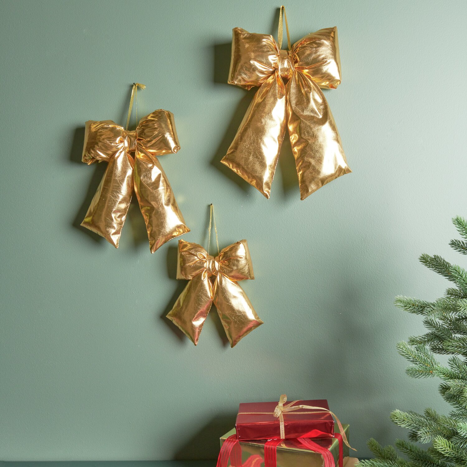 Weihnachtsschleife Gold Größe 36x25x6cm von Rico Design Weihnachtsschleife Gold: Drei glänzende Schleifen von Rico Design an grüner Wand, festlich dekoriert.