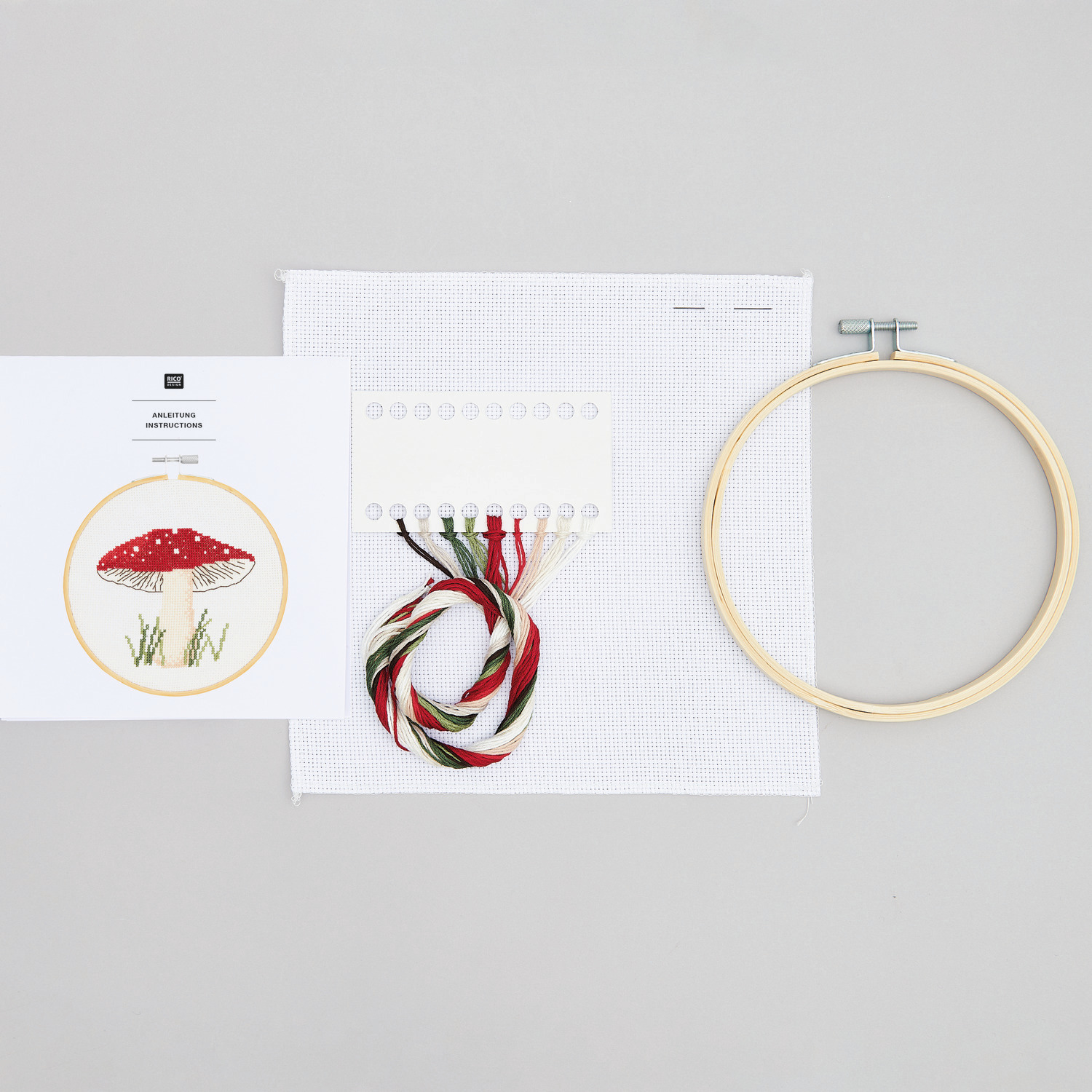 Stickpackung Shrooom Pilz Ø15cm von Rico Design Stickpackung Shrooom Pilz von Rico Design zeigt Stickrahmen, Garn und Vorlage auf grauem Hintergrund. Ideal für kreative Handarbeiten.