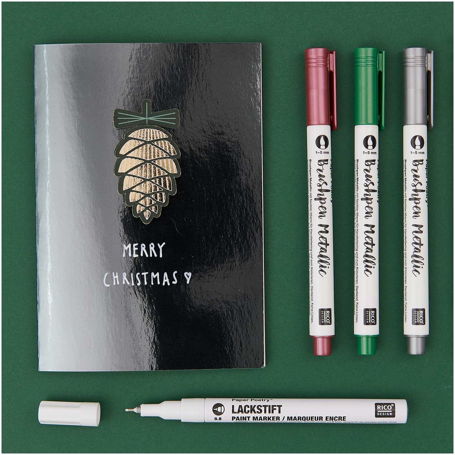 Lackmarker 0,8mm von Rico Design neben einer schwarzen Karte mit Tannenzapfen und drei Brushpen Metallic Stiften.