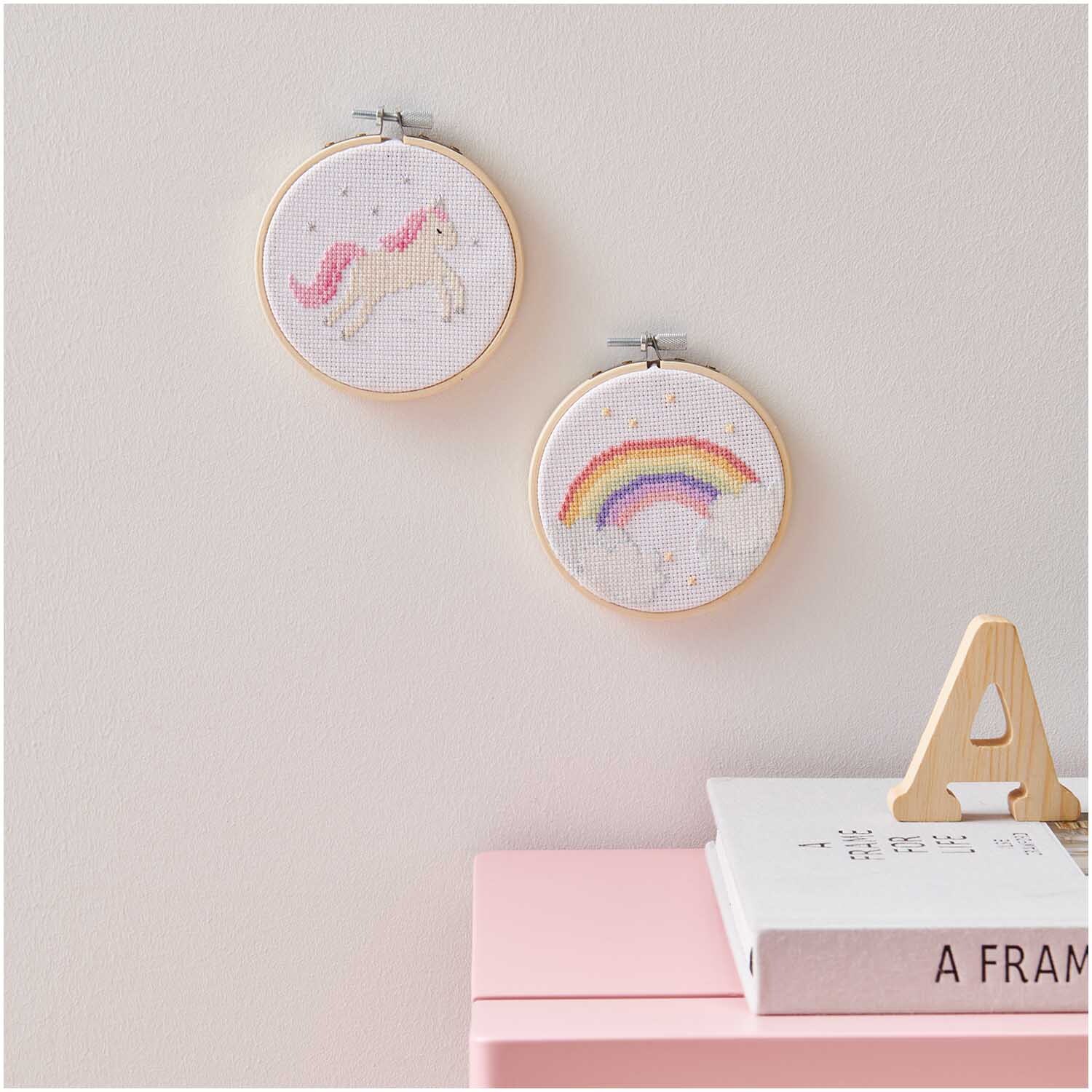 Mini Kit de broderie image licorne Ø 10cm from Rico Design Stickpackung Mini Kit Einhorn Bild Ø 10cm zeigt ein Einhorn und einen Regenbogen in Stickrahmen an der Wand.