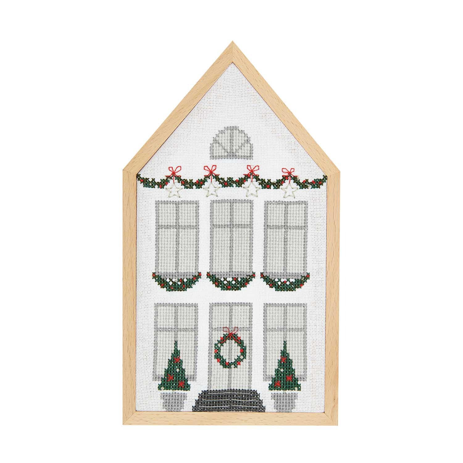 Stickpackung Winterhaus mittel zeigt ein gesticktes Haus mit weihnachtlichen Girlanden und Kränzen. Größe: 12x22,5cm. Marke: Rico Design.