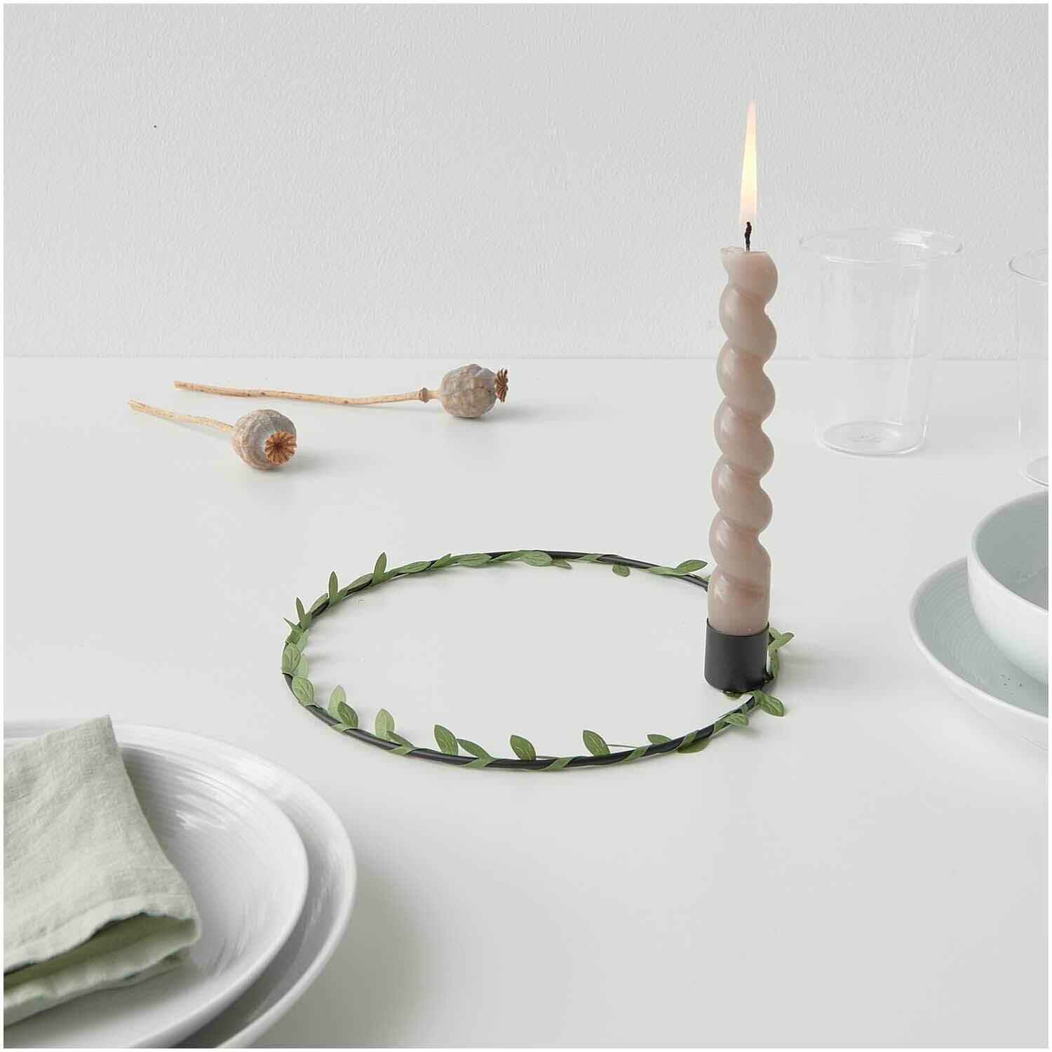 Metallring mit Kerzenhalter Ø 20cm Farbe Schwarz Matt von Rico Design Metallring mit Kerzenhalter Ø 20cm von Rico Design in Schwarz Matt, dekoriert mit grünen Blättern und einer brennenden Kerze auf einem Tisch.