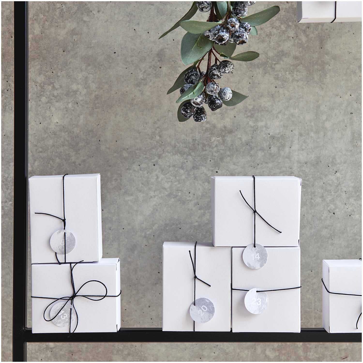 Paper Poetry Adventskalenderanhänger 24 Stück von Rico Design in eleganter Präsentation mit silbernen Details, dekoriert an schlichten, weißen Geschenken.