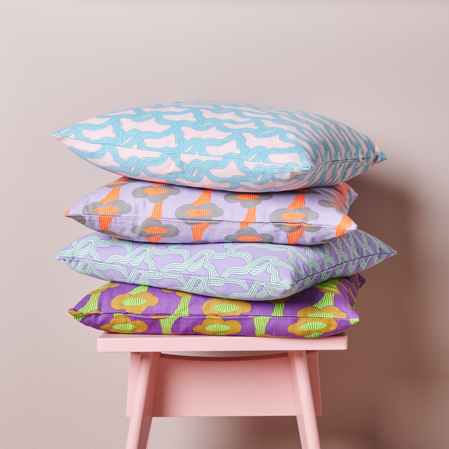 Stoffabschnitt Canvas Pfifferlinge Neon Violett 50x140cm von Rico Design Stoffabschnitt Canvas Pfifferlinge Neon Violett: Vier bunte Kissen mit Pilz- und Myzelmustern von Rico Design auf einem rosa Stuhl.